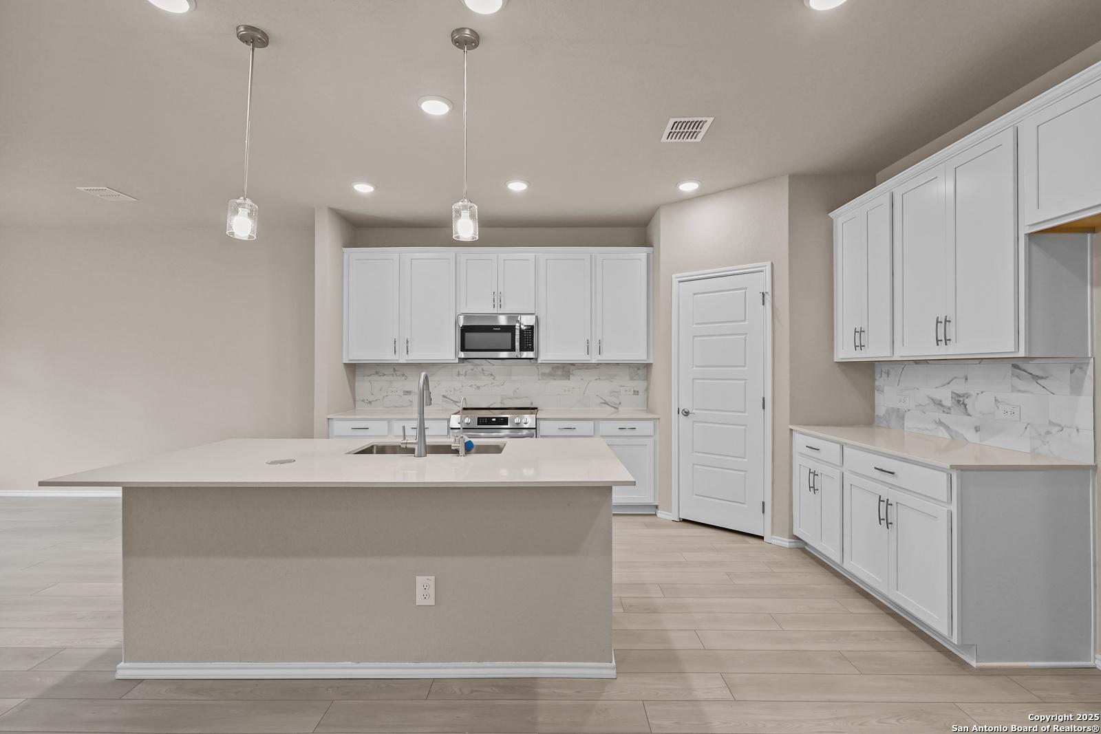 Modern white kitchen with large island, stainless appliances, quartz counters in Davidson Homes The Douglas G, San Antonio