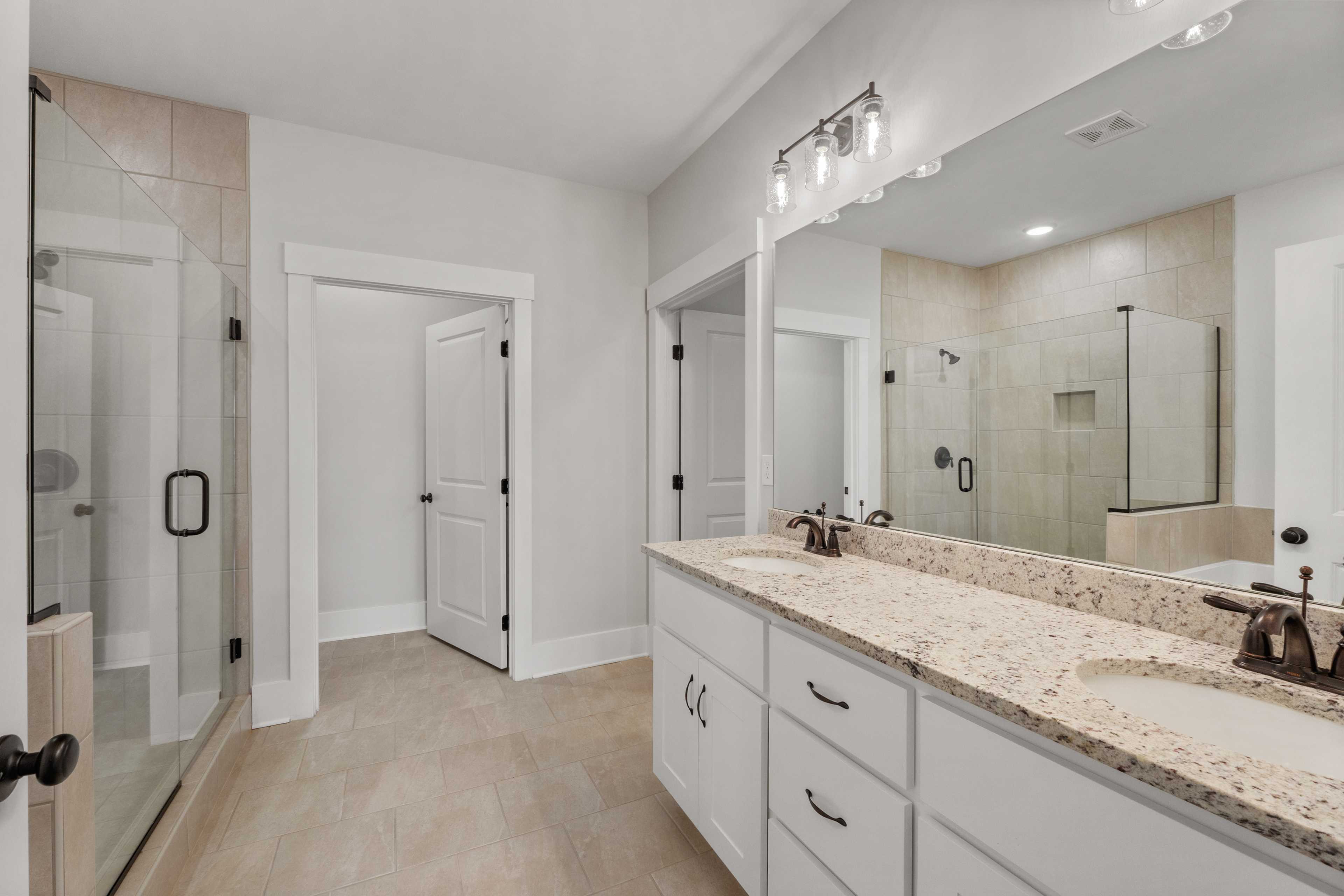Spacious primary bathroom at The Villas at Barnett's Crossing in Madison, Alabama with double vanity, frameless glass shower, and neutral tile