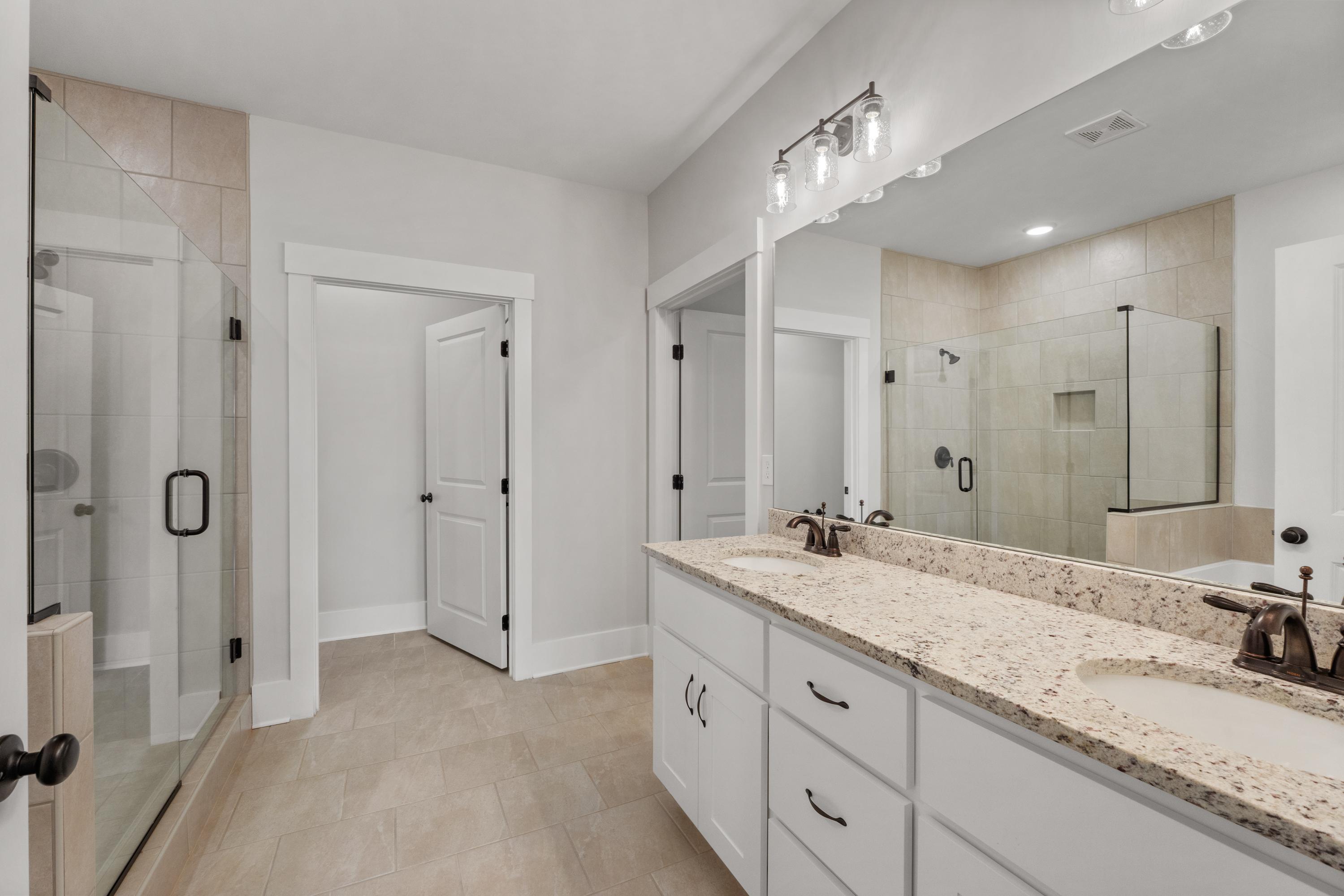 Spacious primary bathroom at The Villas at Barnett's Crossing in Madison, Alabama with double vanity, frameless glass shower, and neutral tile