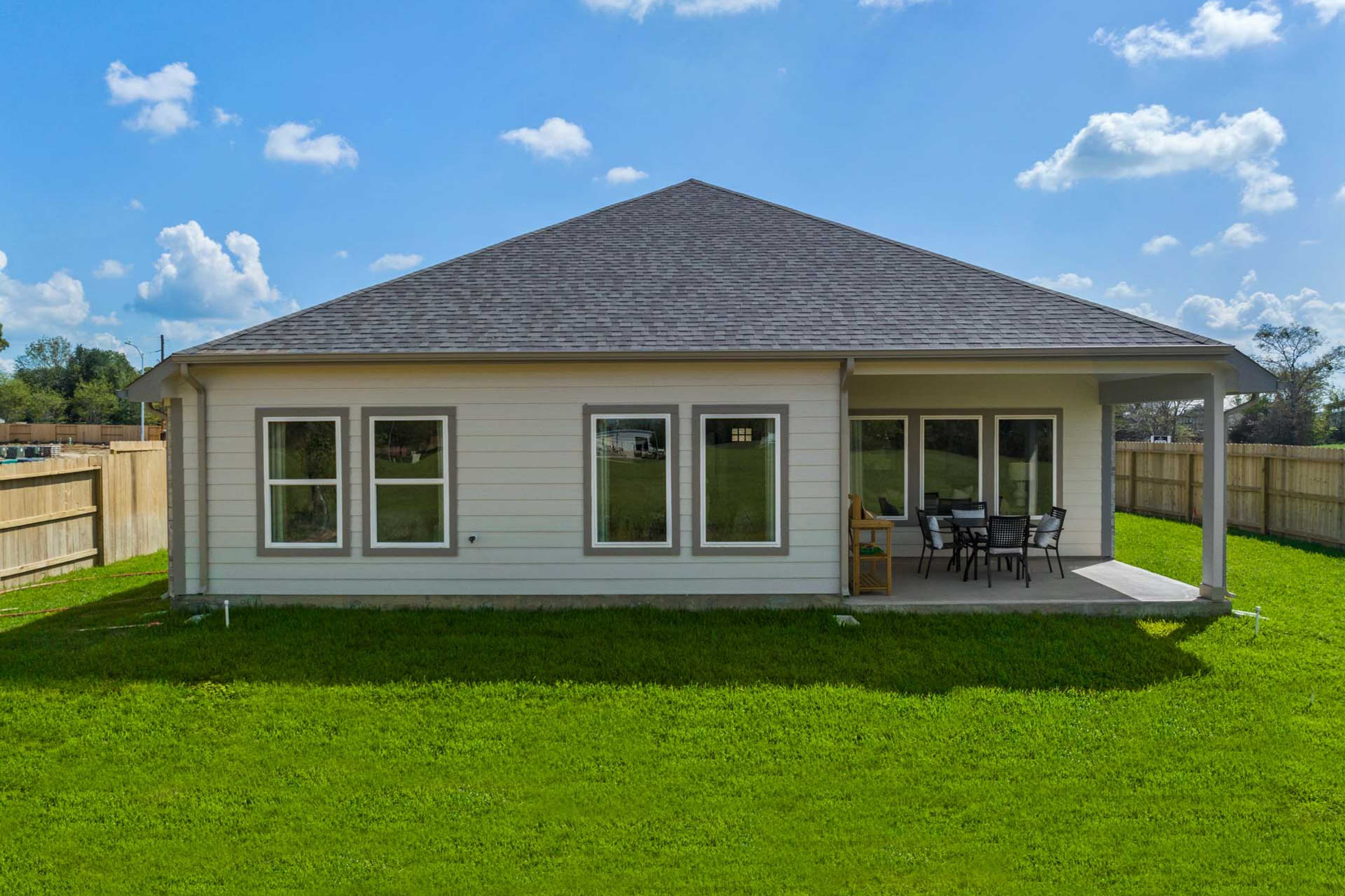 Back view of single-story home at Windmill Estates in Magnolia Texas with covered patio, large windows, patio furniture, and lush green yard