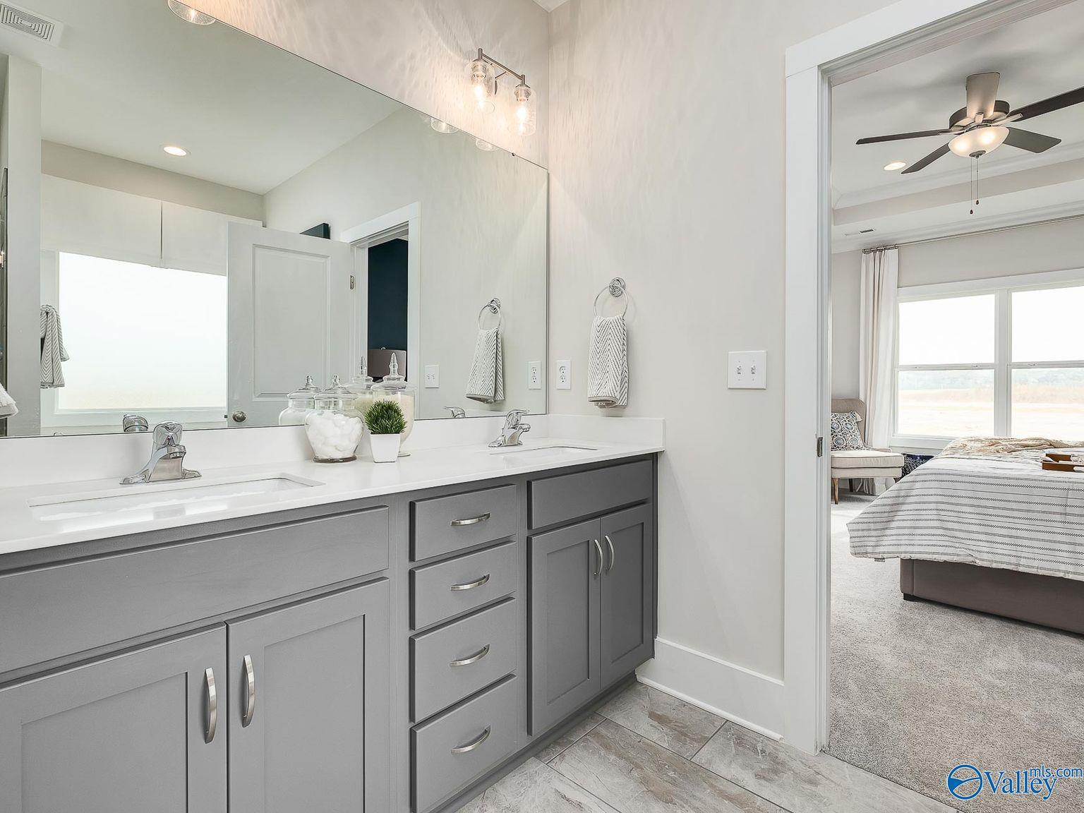 Elegant master bathroom with double gray vanity, large mirror, and open view to bedroom in Davidson Homes The Everett, Toney, Alabama
