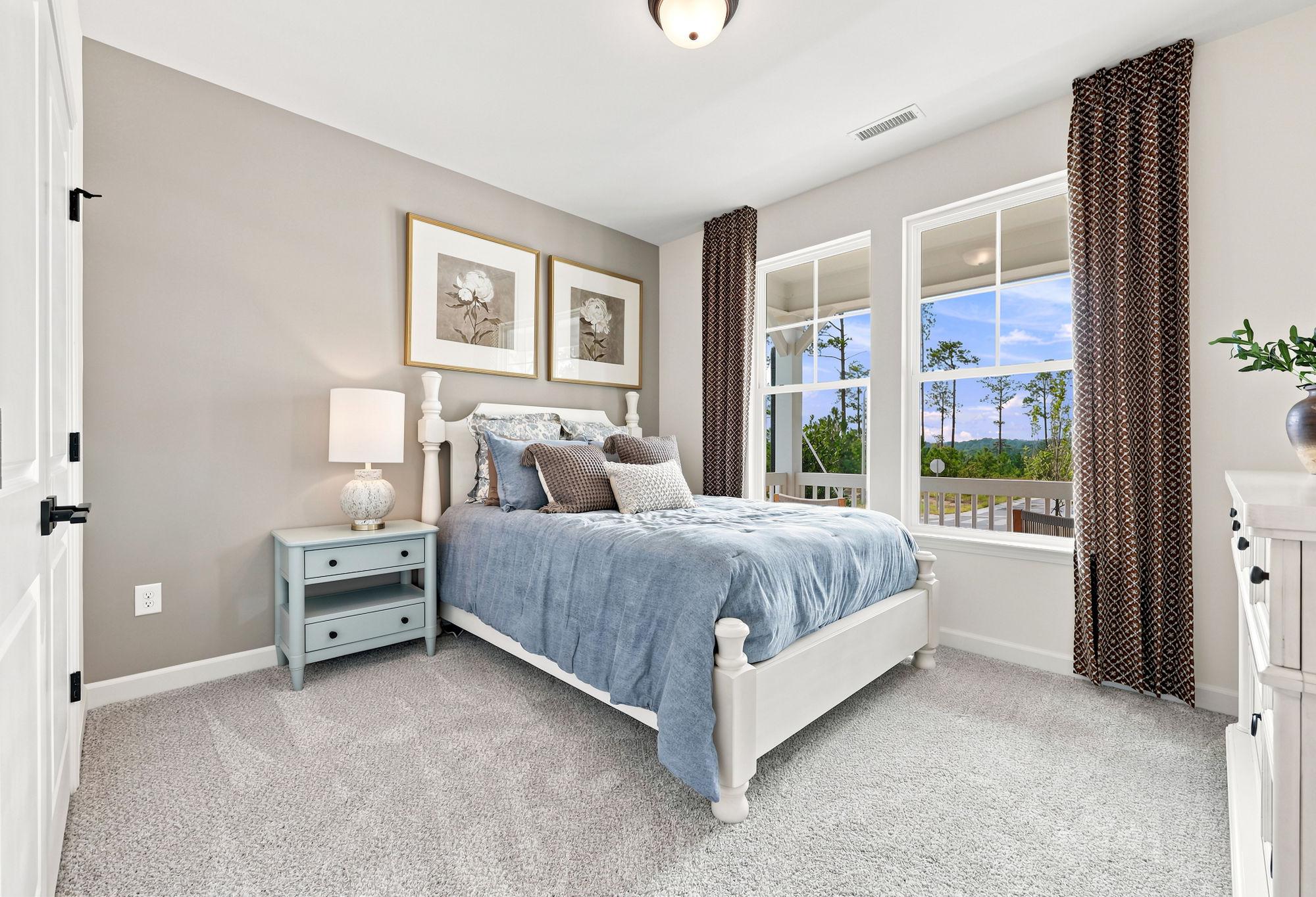 Cozy secondary bedroom in The Beech by Davidson Homes featuring a white bed frame, blue bedding, and large windows.