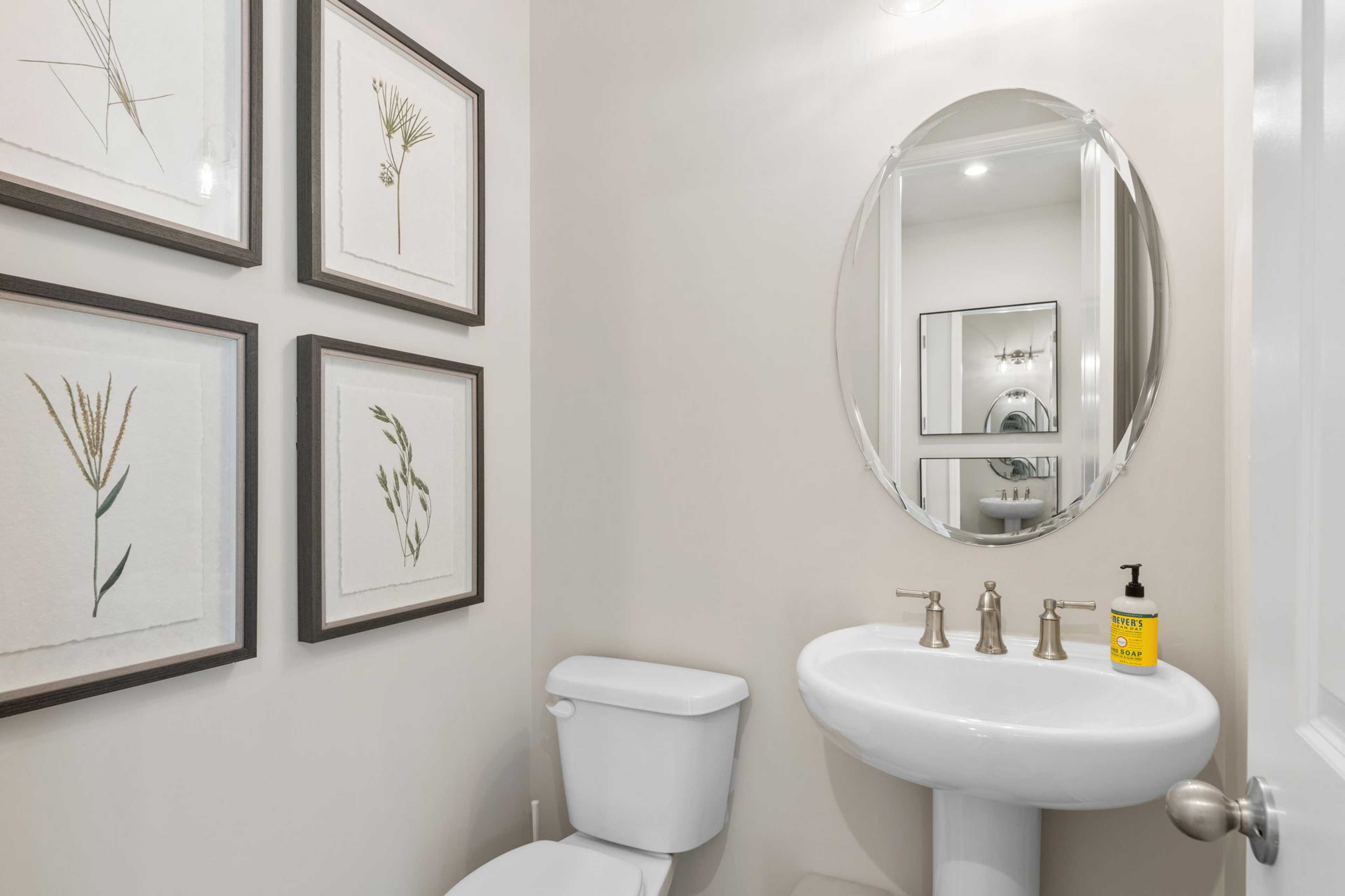 Elegant powder room in Melody Lakeside Estates, Buford GA with pedestal sink, round mirror, and botanical art by Davidson Homes