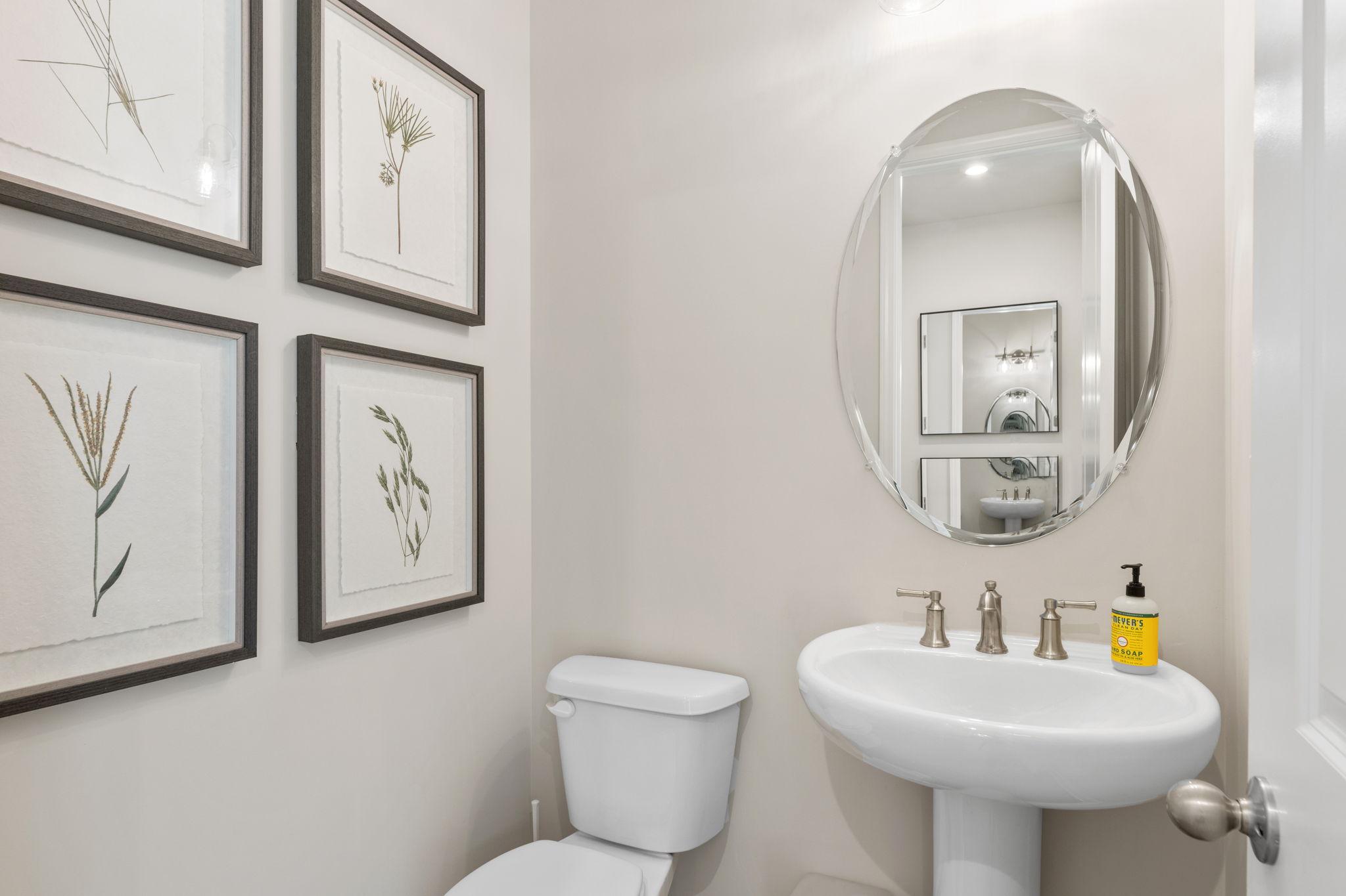 Elegant powder room in Melody Lakeside Estates, Buford GA with pedestal sink, round mirror, and botanical art by Davidson Homes