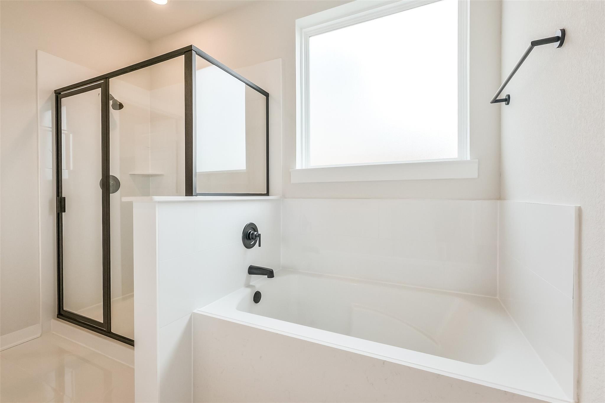 Modern master bathroom featuring frameless glass shower, deep soaking tub, and white subway tiles in Davidson Homes The Tierra B, Beasley, Texas
