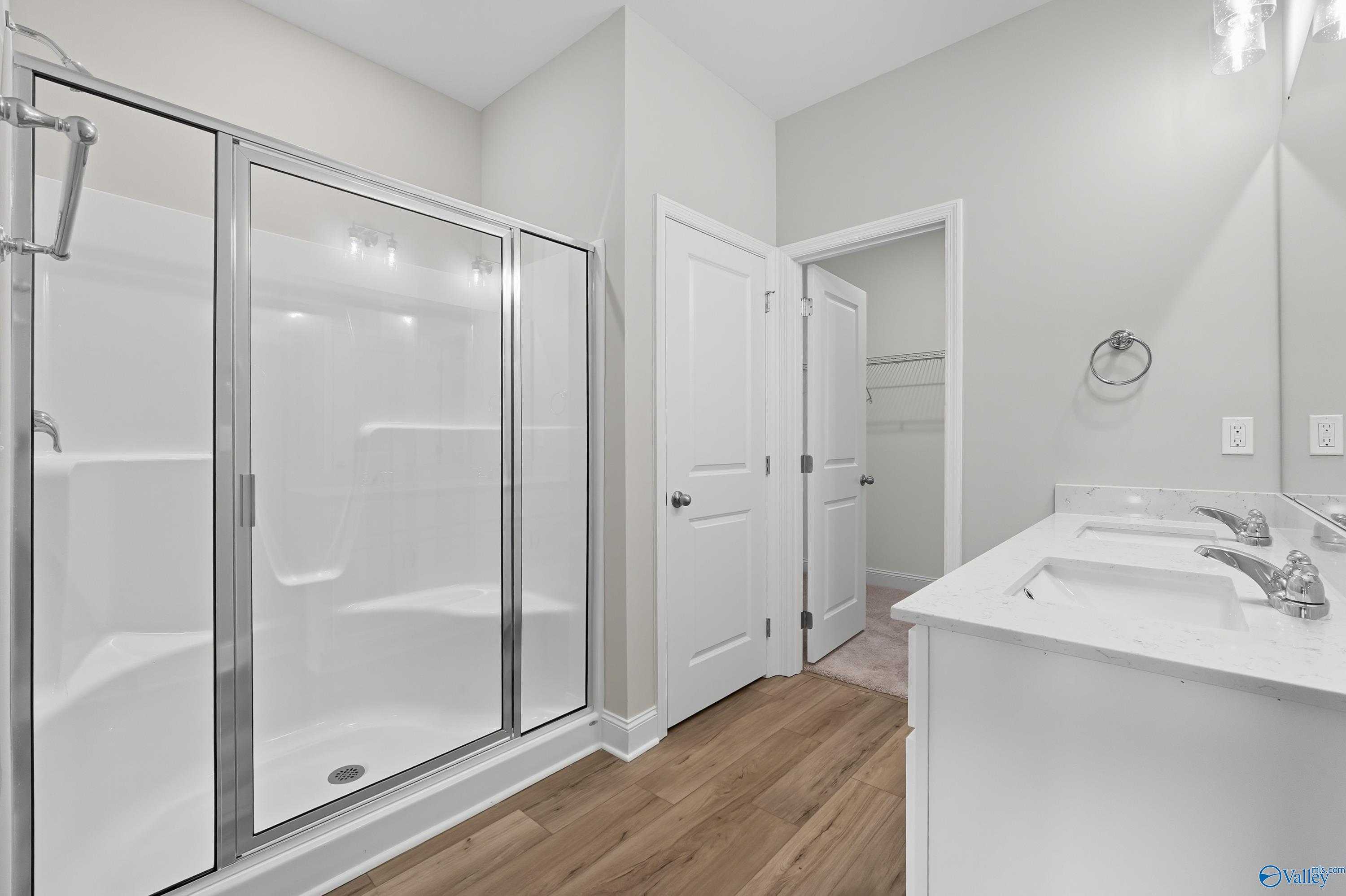 Modern master bathroom with glass-enclosed shower, double white vanity, and wood flooring in Davidson Homes The Franklin, Meridianville, Alabama