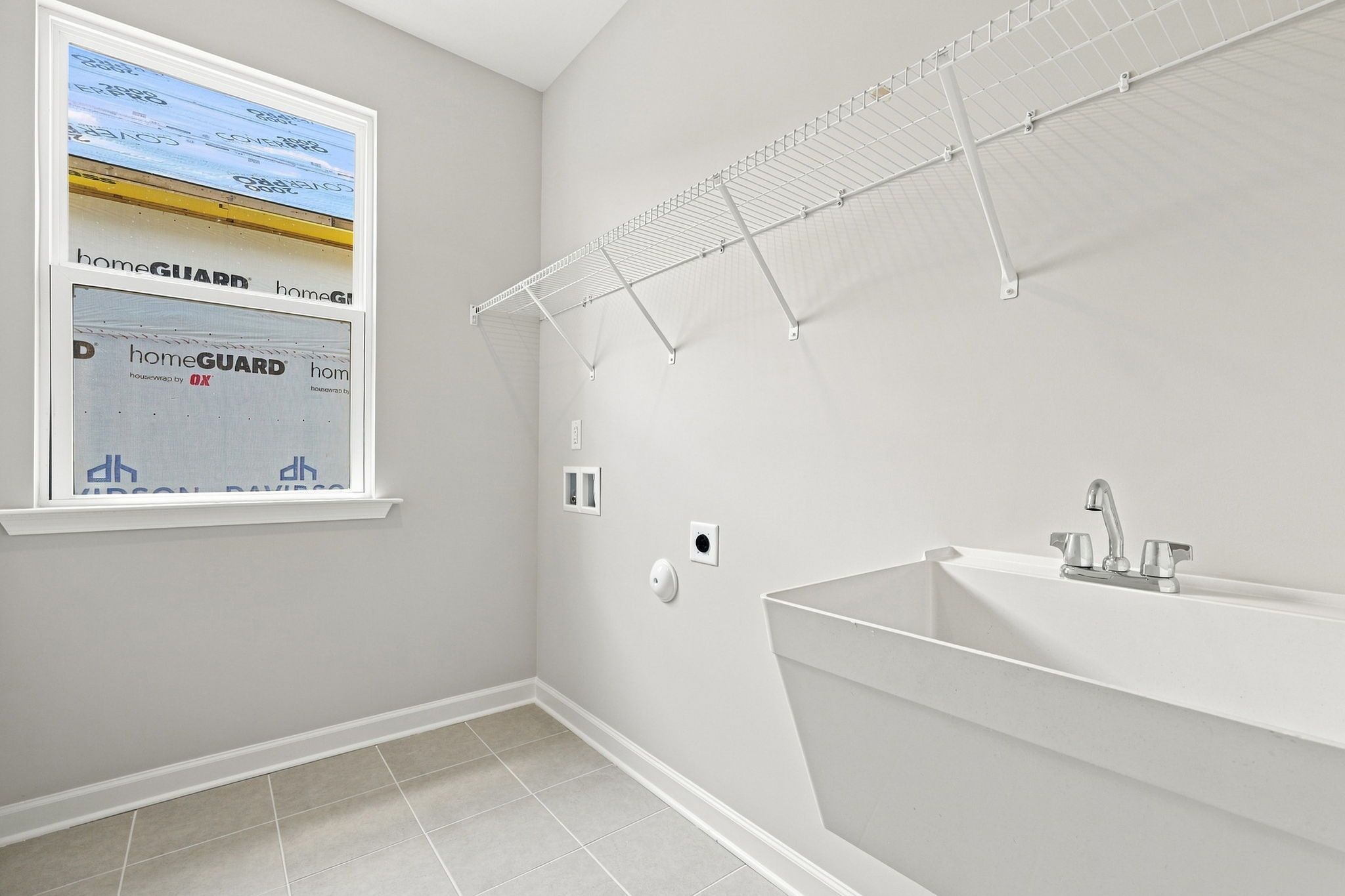 Laundry room in The Jordan A featuring a utility sink, wire shelving, and tile flooring in a new Knightdale home.