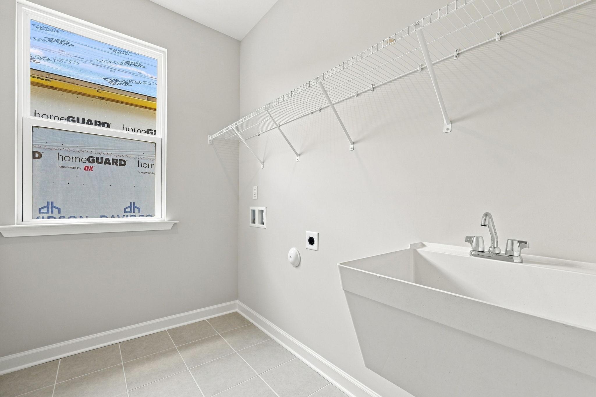 Laundry room in The Jordan A featuring a utility sink, wire shelving, and tile flooring in a new Knightdale home.