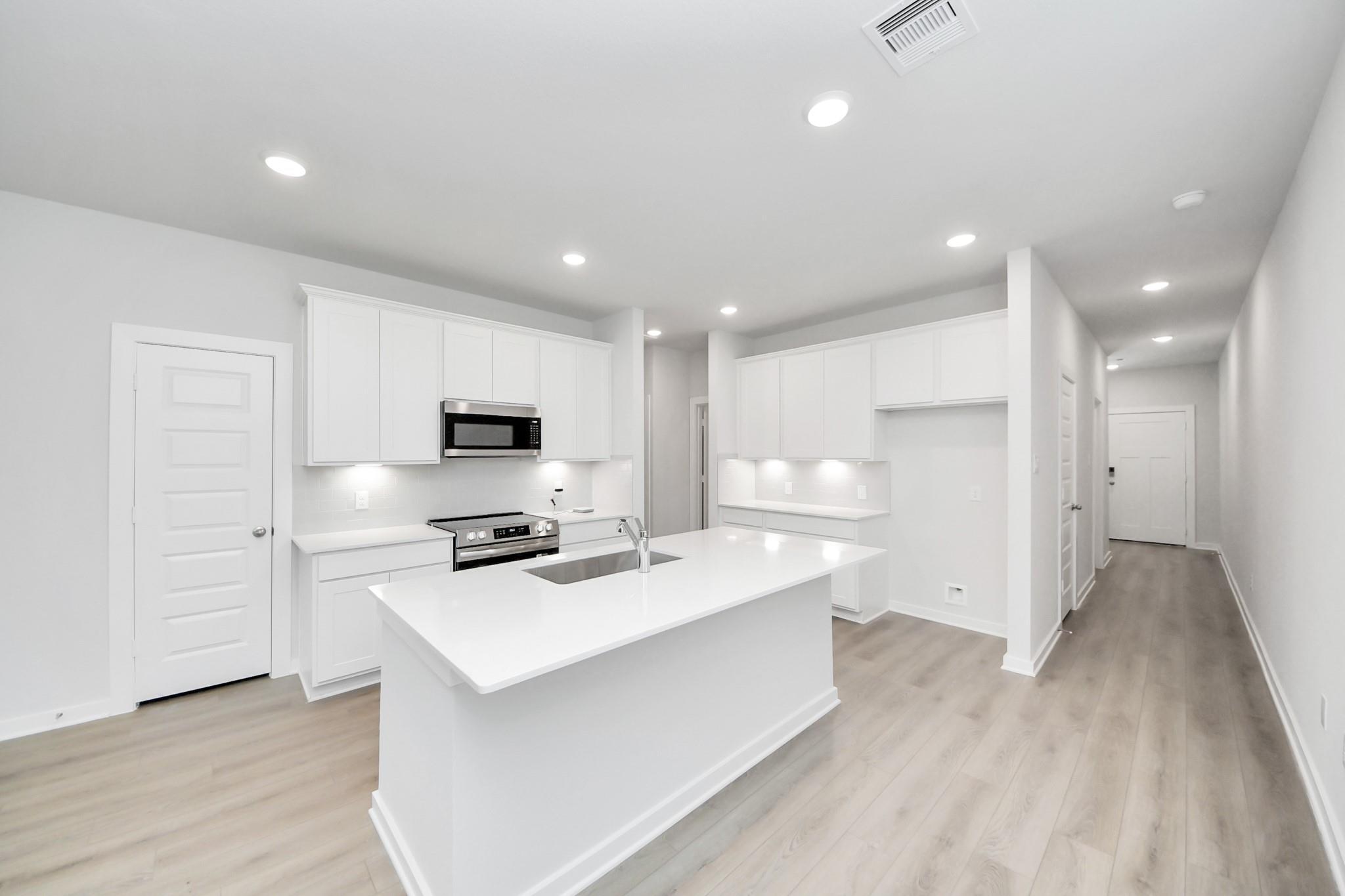 Modern kitchen with white cabinets, quartz island, and stainless appliances in The Frio F home at Liberty Estates, Texas.