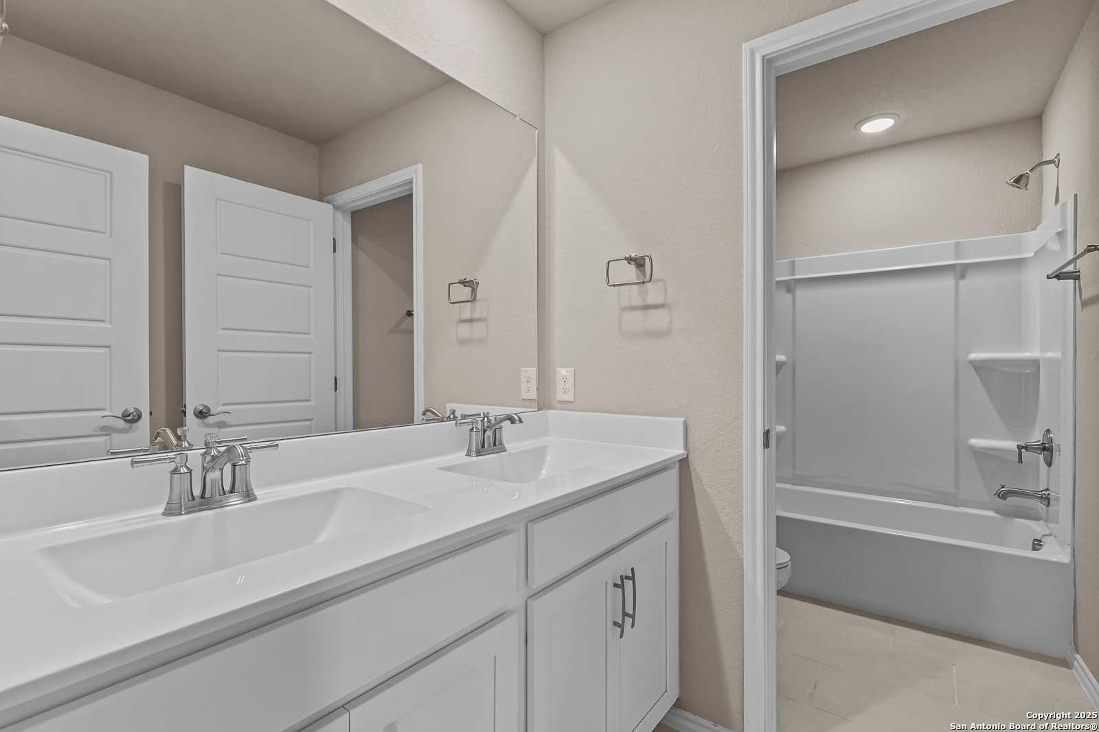 Modern bathroom with double vanity, white cabinets, and tub/shower combo in Davidson Homes The Douglas G, San Antonio