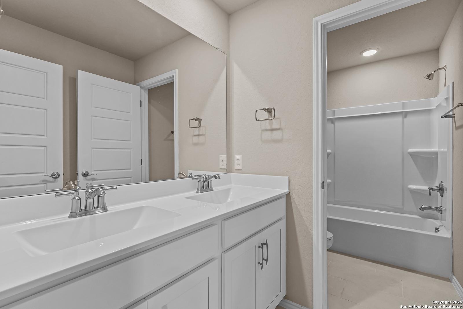 Modern bathroom with double vanity, white cabinets, and tub/shower combo in Davidson Homes The Douglas G, San Antonio