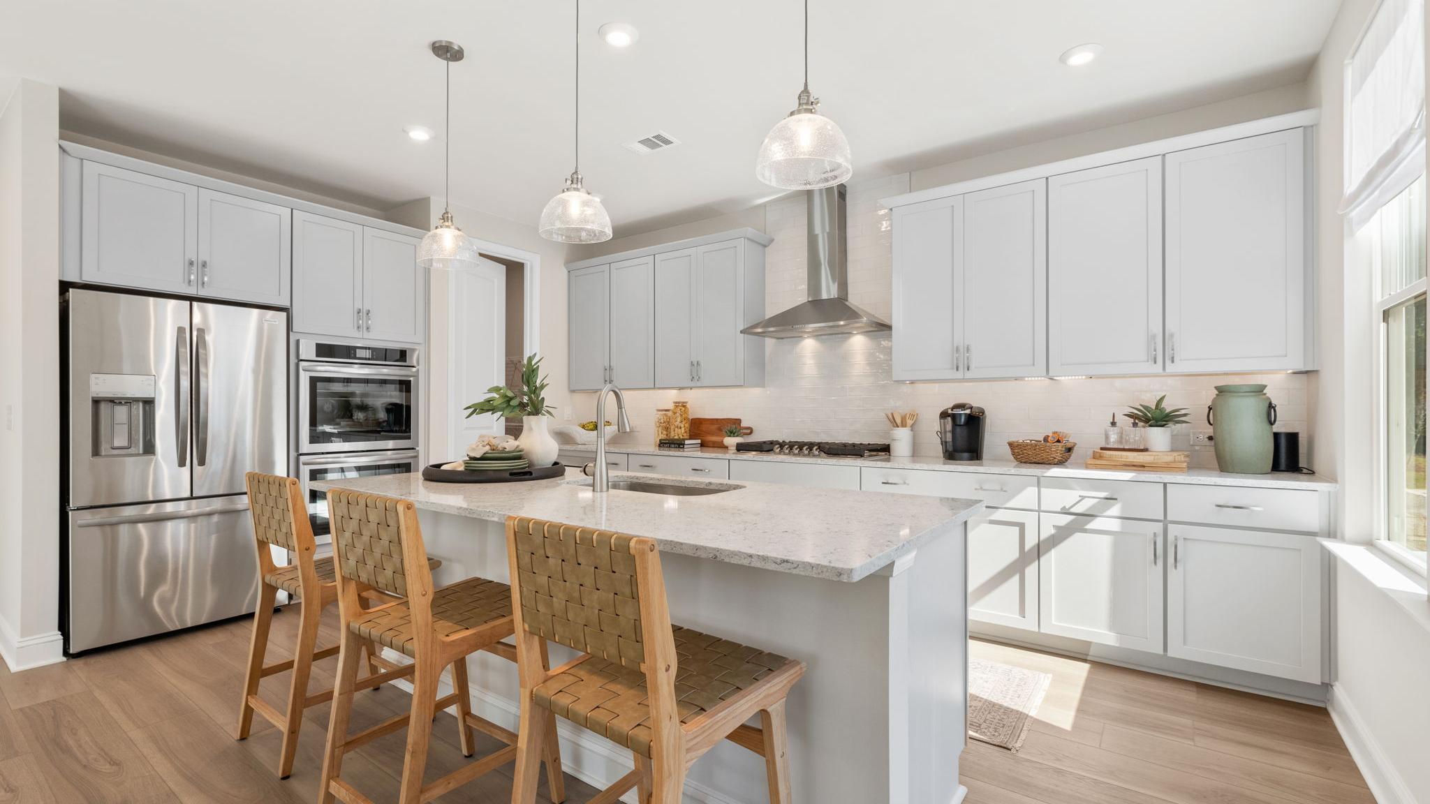 Spacious modern kitchen at Melody Lakeside Estates in Buford GA with white cabinets, large island seating, stainless appliances, hardwood floors