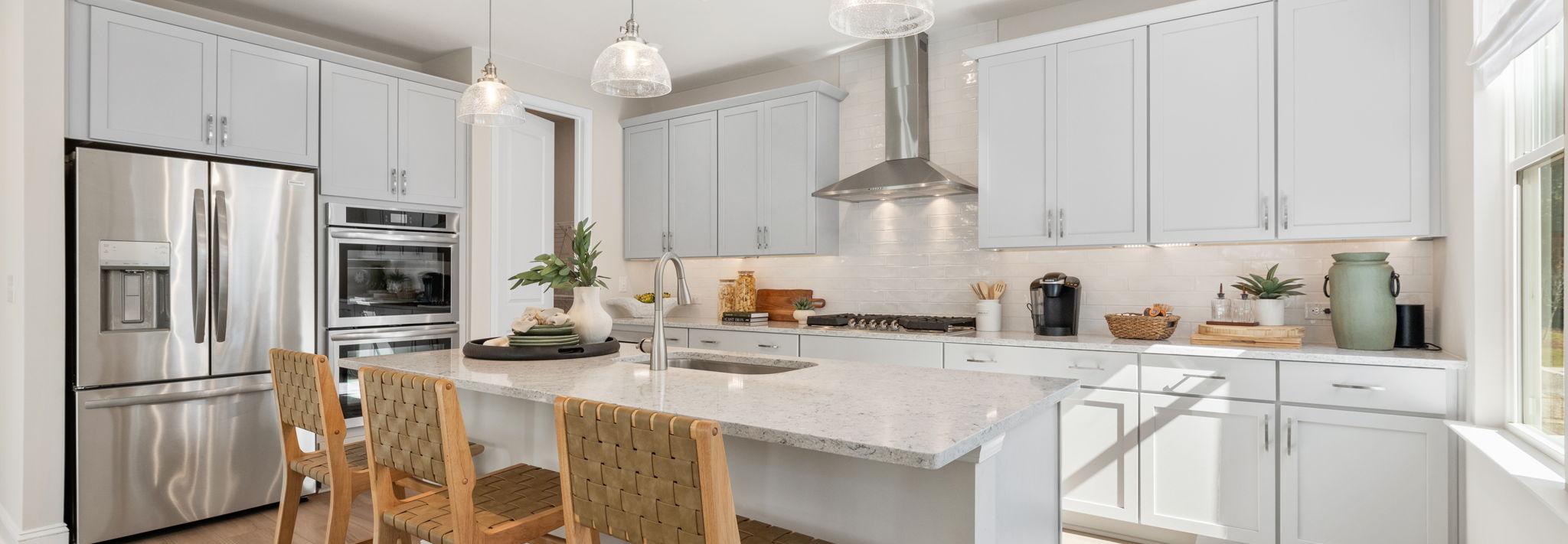 Spacious modern kitchen at Melody Lakeside Estates in Buford GA with white cabinets, large island seating, stainless appliances, hardwood floors