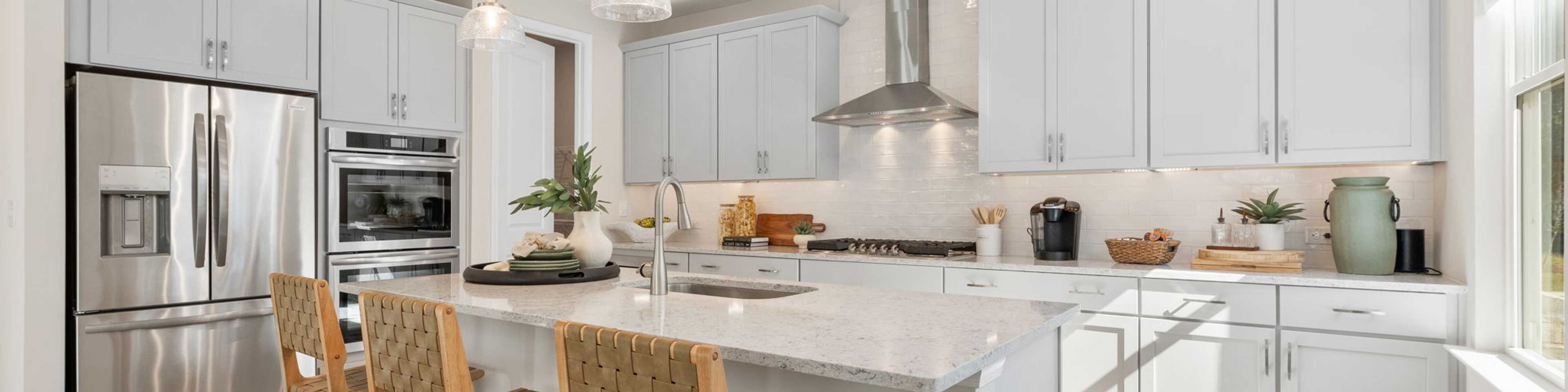 Spacious modern kitchen at Melody Lakeside Estates in Buford GA with white cabinets, large island seating, stainless appliances, hardwood floors