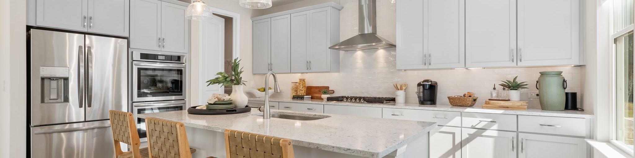 Spacious modern kitchen at Melody Lakeside Estates in Buford GA with white cabinets, large island seating, stainless appliances, hardwood floors