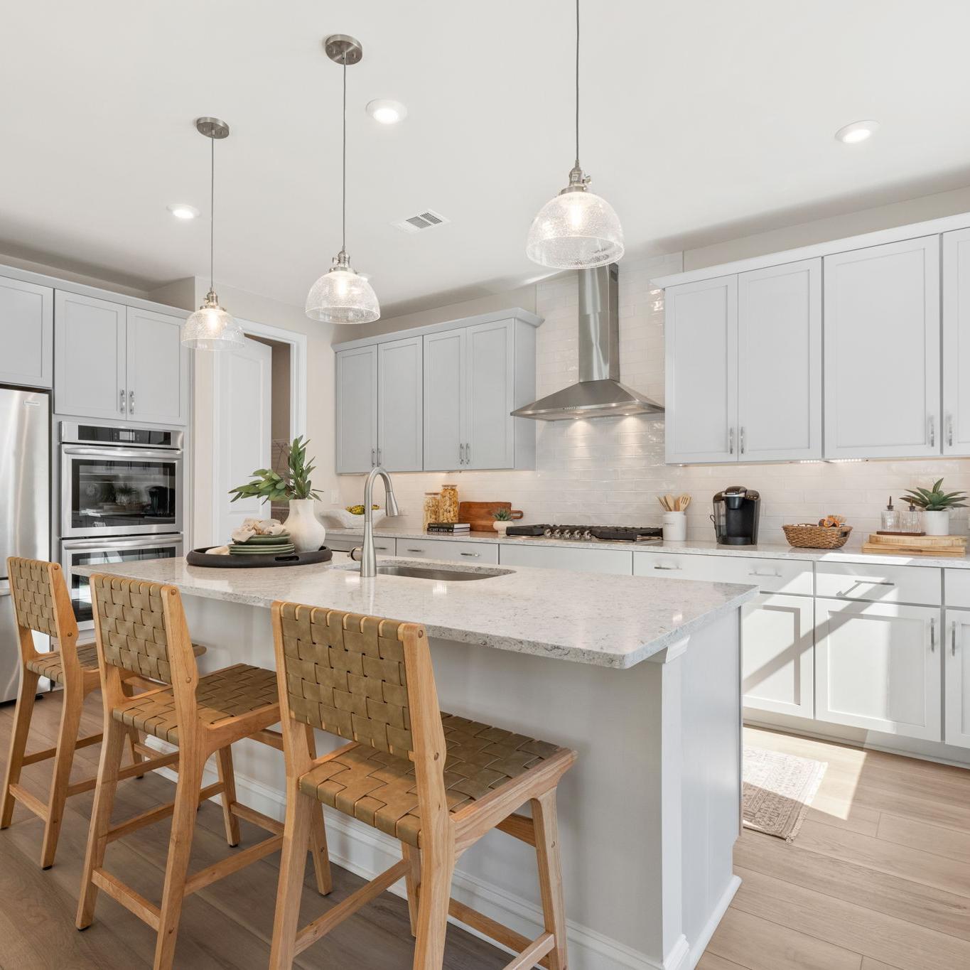 Spacious modern kitchen at Melody Lakeside Estates in Buford GA with white cabinets, large island seating, stainless appliances, hardwood floors