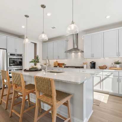 Spacious modern kitchen at Melody Lakeside Estates in Buford GA with white cabinets, large island seating, stainless appliances, hardwood floors