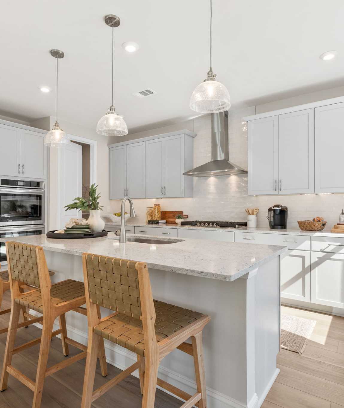 Spacious modern kitchen at Melody Lakeside Estates in Buford GA with white cabinets, large island seating, stainless appliances, hardwood floors