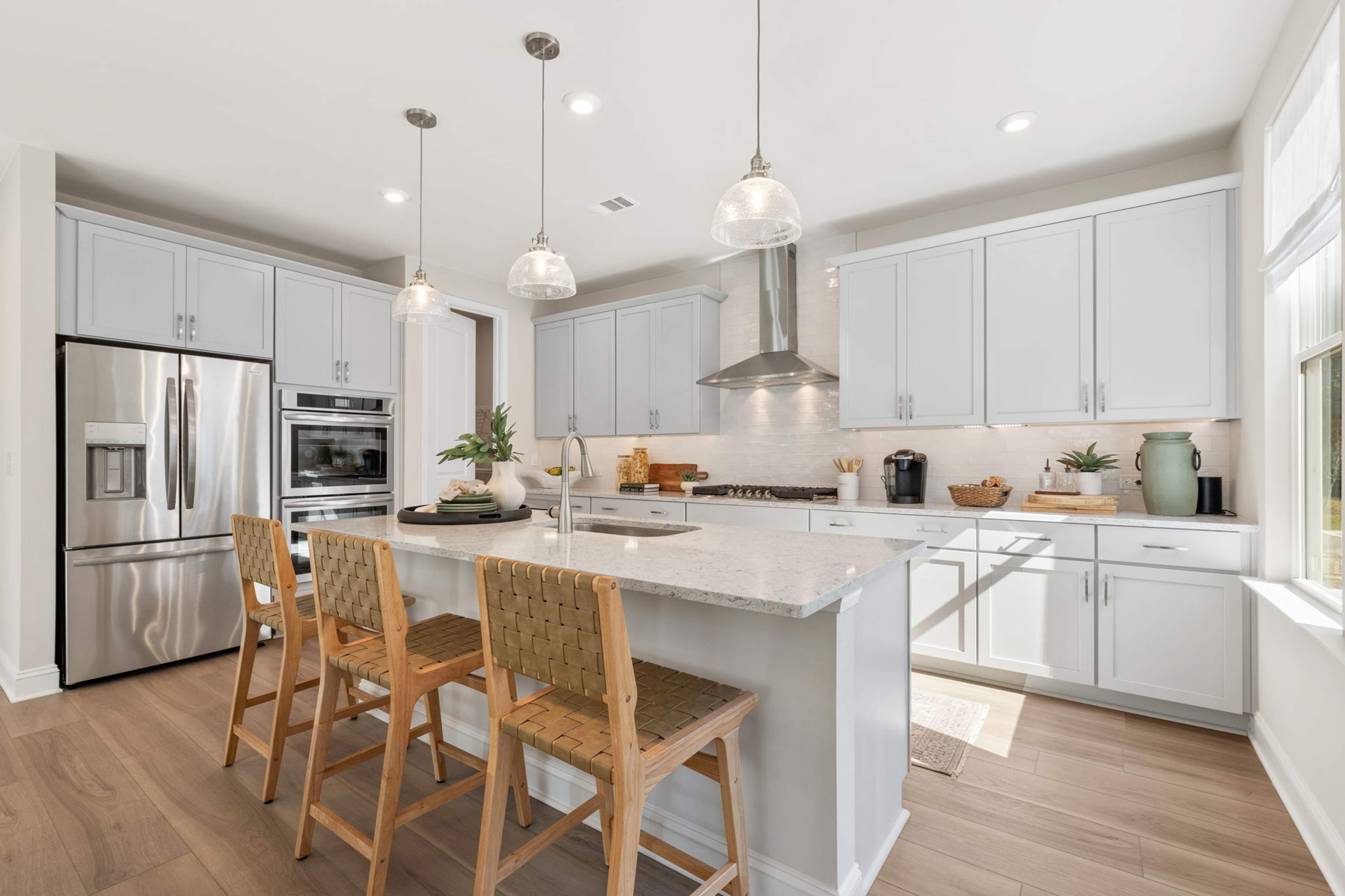 Spacious modern kitchen at Melody Lakeside Estates in Buford GA with white cabinets, large island seating, stainless appliances, hardwood floors