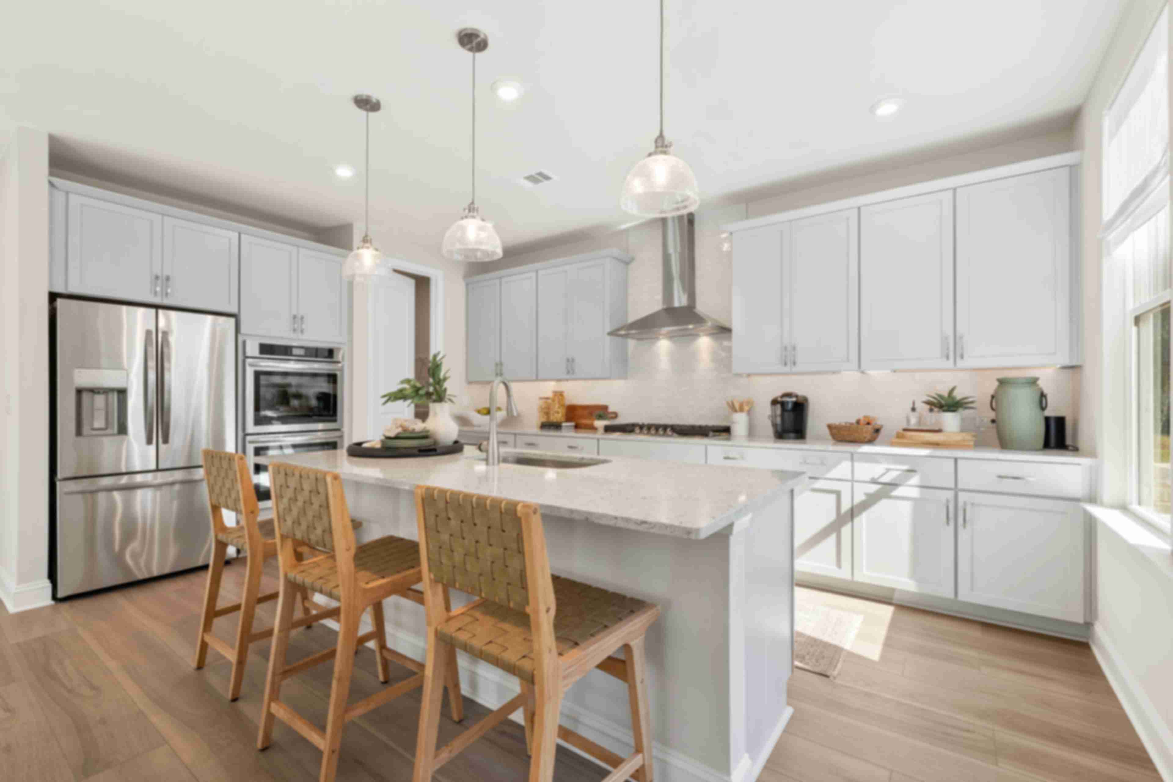 Spacious modern kitchen at Melody Lakeside Estates in Buford GA with white cabinets, large island seating, stainless appliances, hardwood floors
