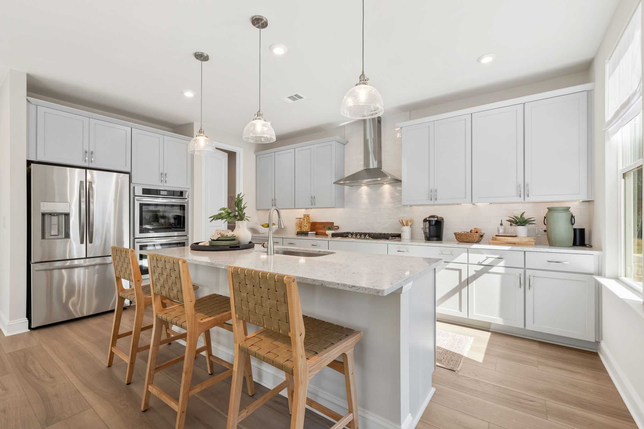 Spacious modern kitchen at Melody Lakeside Estates in Buford GA with white cabinets, large island seating, stainless appliances, hardwood floors