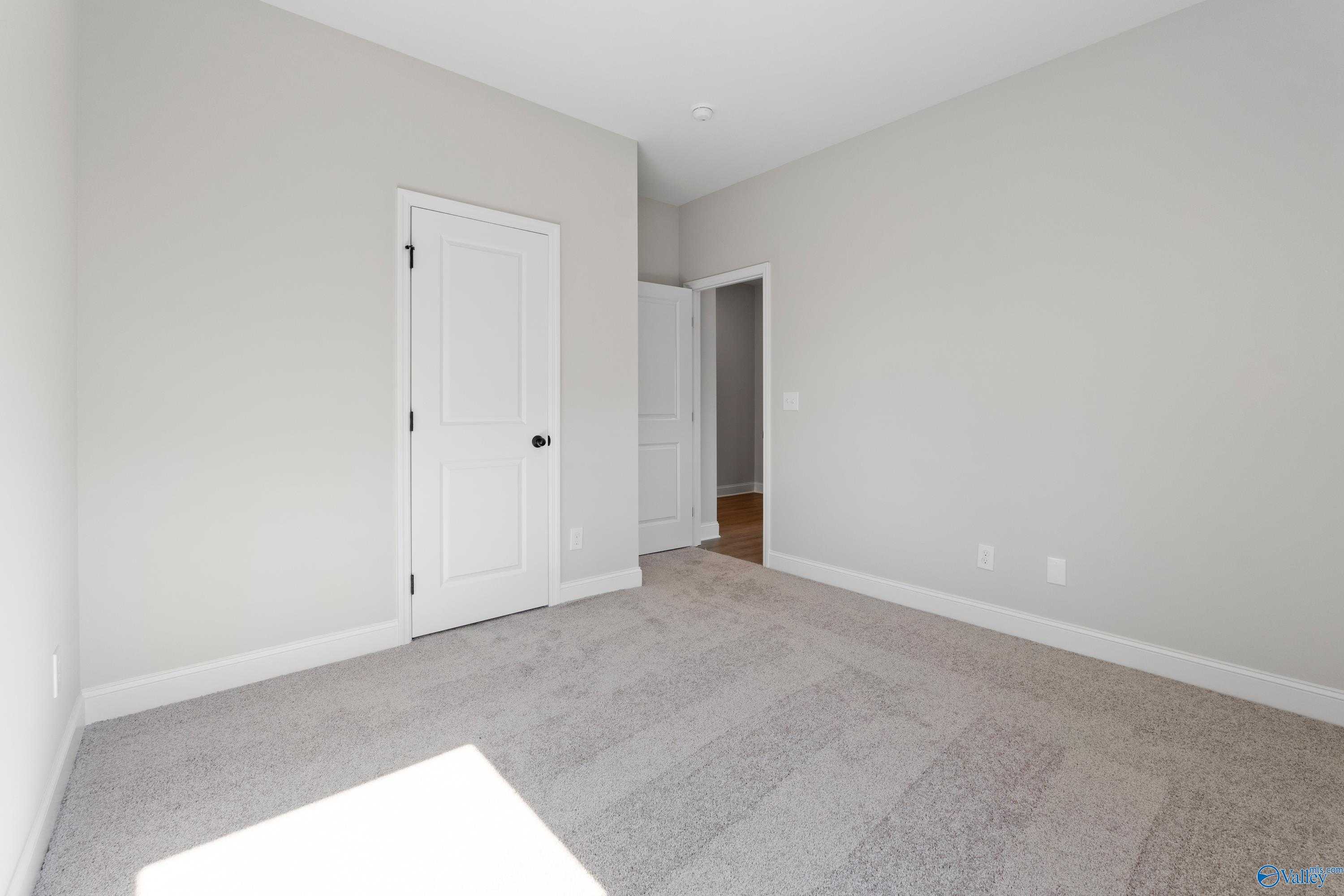 Bright secondary bedroom with neutral gray walls, beige carpet, white doors in Davidson Homes The Franklin C, Hazel Green, AL