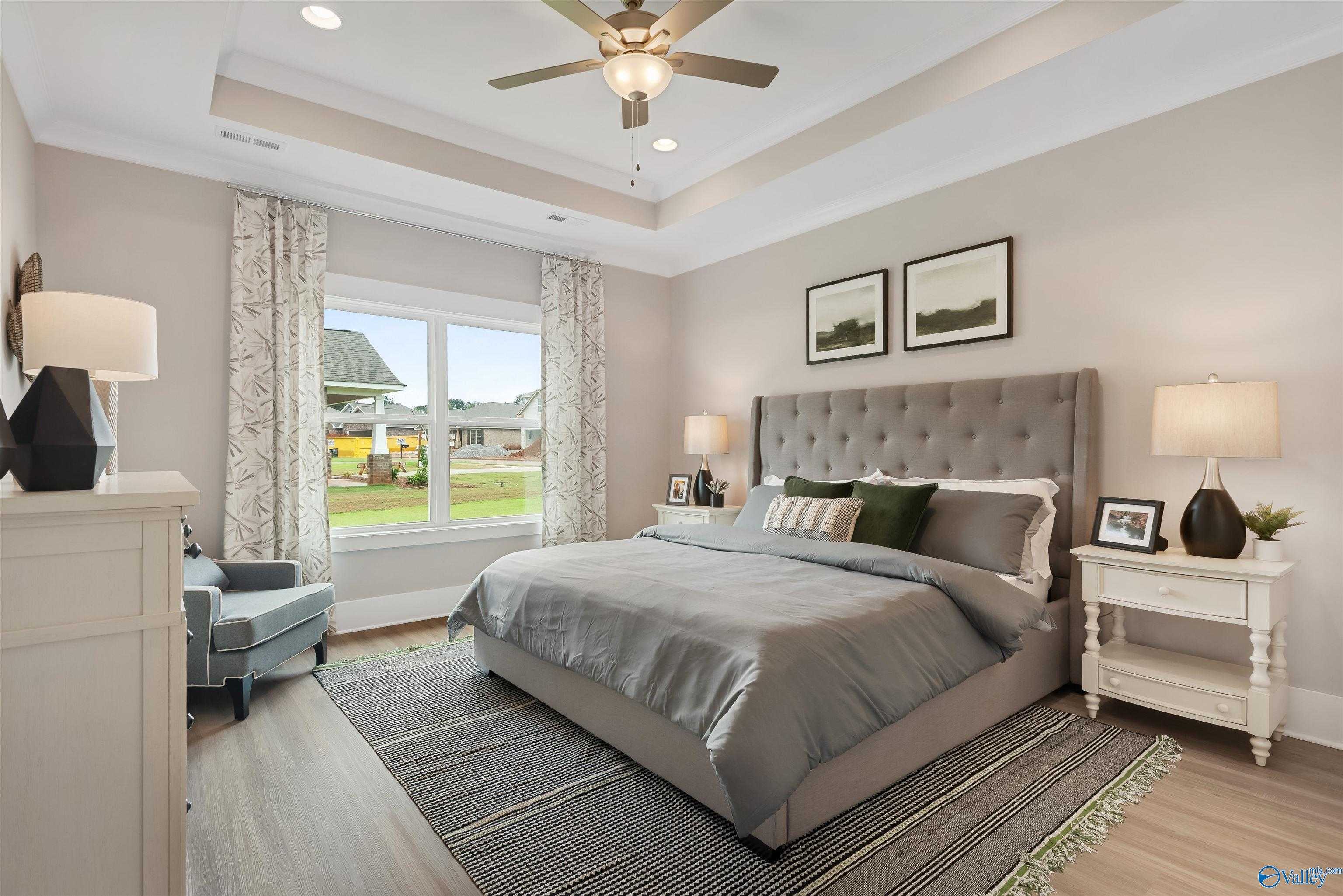 Elegant master bedroom with gray tufted bed, ceiling fan, and garden view in Davidson Homes The Daphne, Harvest, Alabama