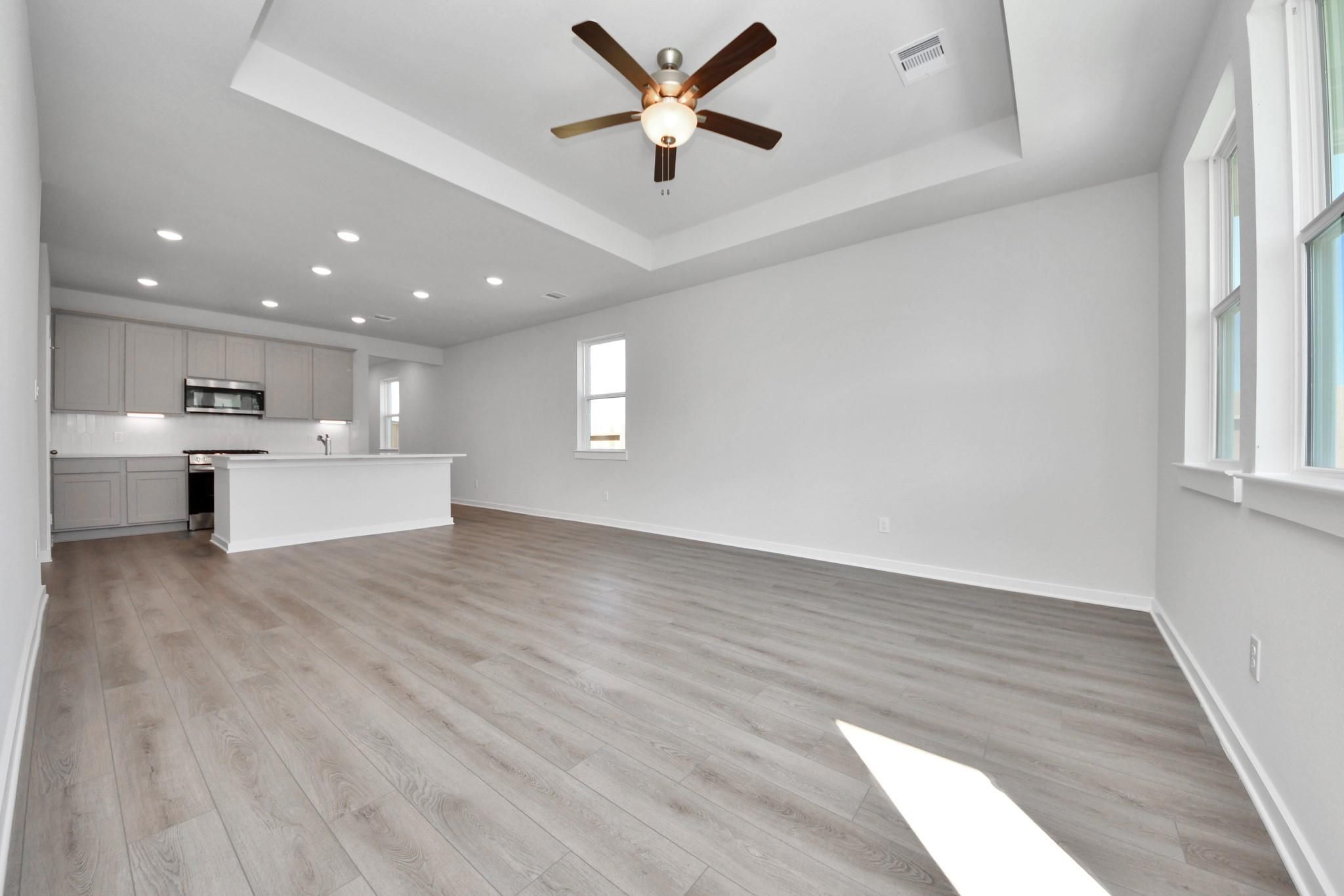 Open-concept living room with tray ceiling and kitchen in The Colorado G floor plan at Emberly, Beasley, Texas.