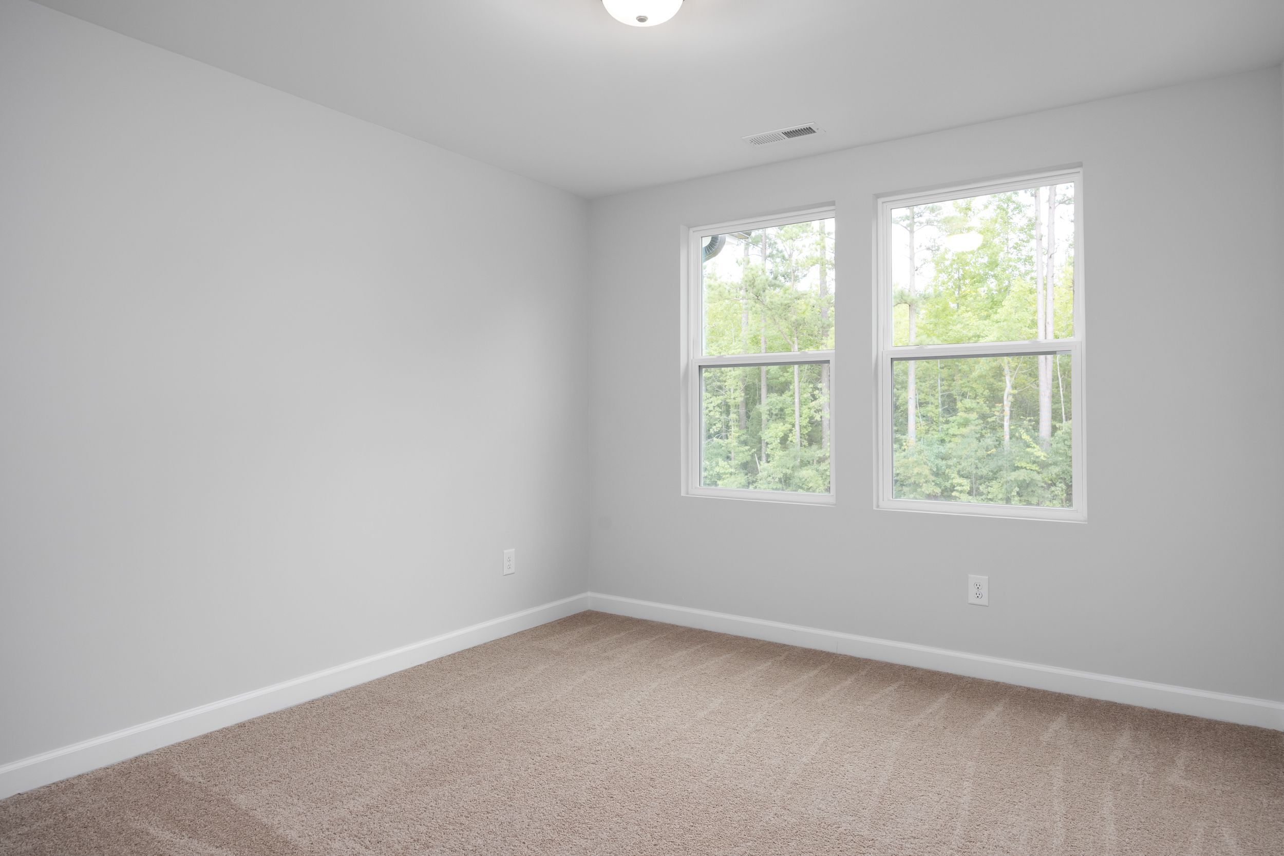 Bright, carpeted bedroom in The Warren home design by Davidson Homes, featuring neutral walls and scenic window views.
