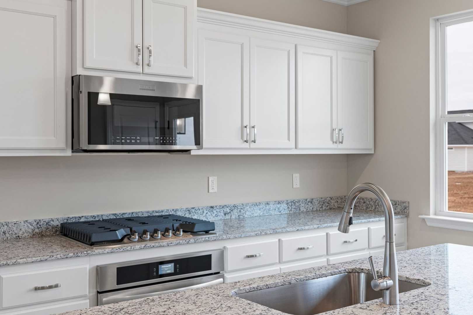 Spacious kitchen in The Stella home with white shaker cabinets, granite countertops, stainless steel appliances, and window view