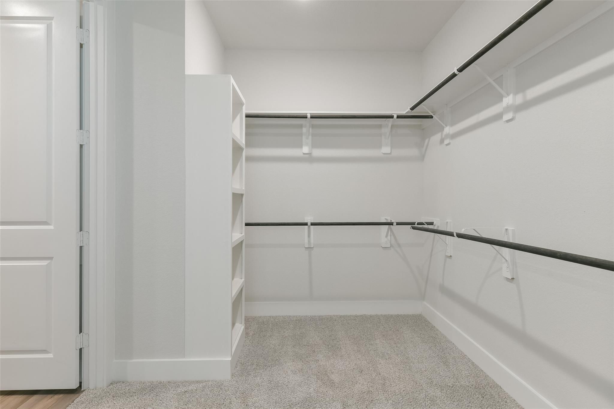 Spacious empty walk-in closet with white walls, built-in shelves and hanging rods in Davidson Homes The Edward A, Lago Mar, Texas City