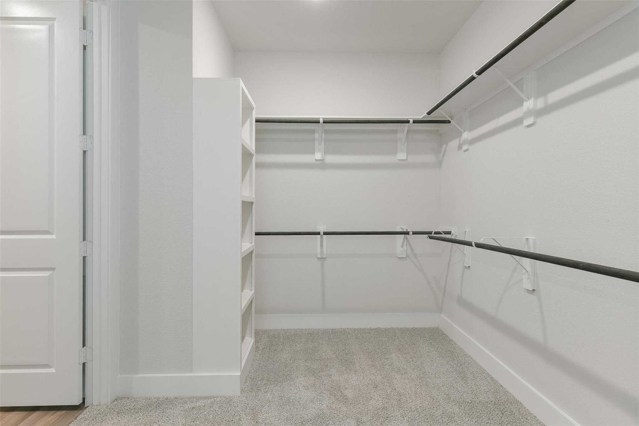 Spacious empty walk-in closet with white walls, built-in shelves and hanging rods in Davidson Homes The Edward A, Lago Mar, Texas City