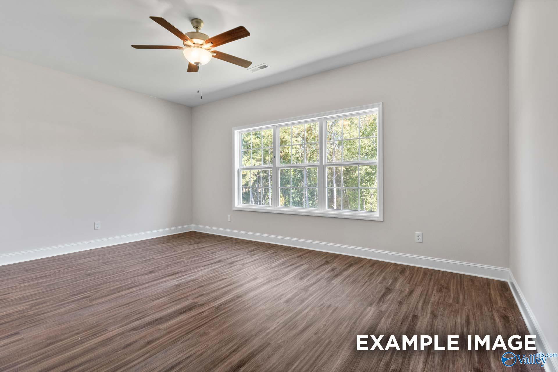 Bright empty bedroom featuring hardwood floors, large window with wooded view, and ceiling fan in The Montgomery C, Harvest, AL