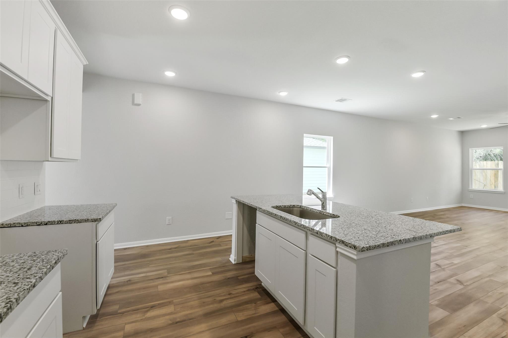 Modern white kitchen with granite countertops, center island sink, and hardwood floors in Davidson Homes The Sabine E, Conroe, Texas