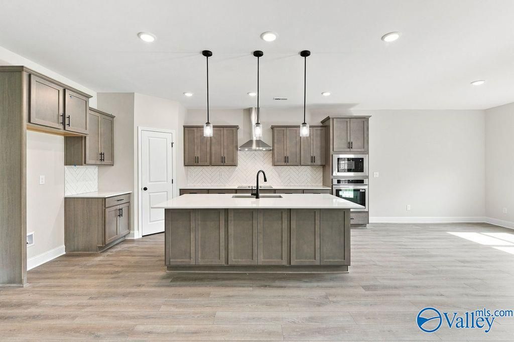 Kitchen island with pendant lights, gray cabinetry, and luxury vinyl plank flooring in Davidson Homes Rockford plan, Hartselle, AL