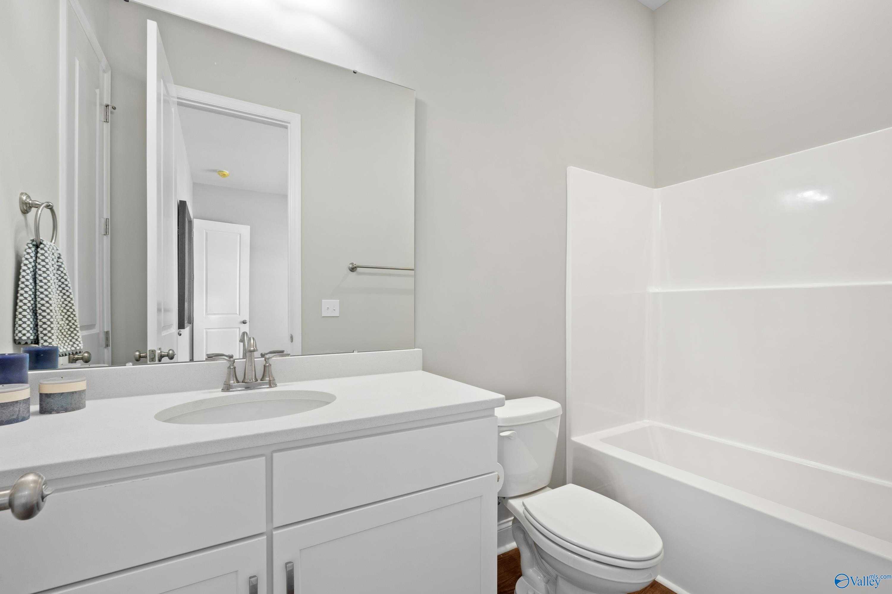 Bright guest bathroom with white vanity, mirror, tub-shower combo, and toilet in Evermore Homes The Haven, Owens Cross Roads, AL