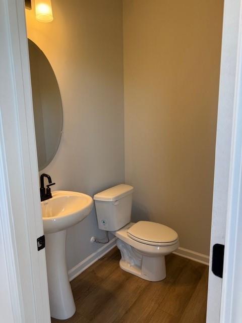 Elegant powder room featuring white pedestal sink, round mirror, toilet, and hardwood floors in Davidson Homes The Durham B, Cumming, Georgia
