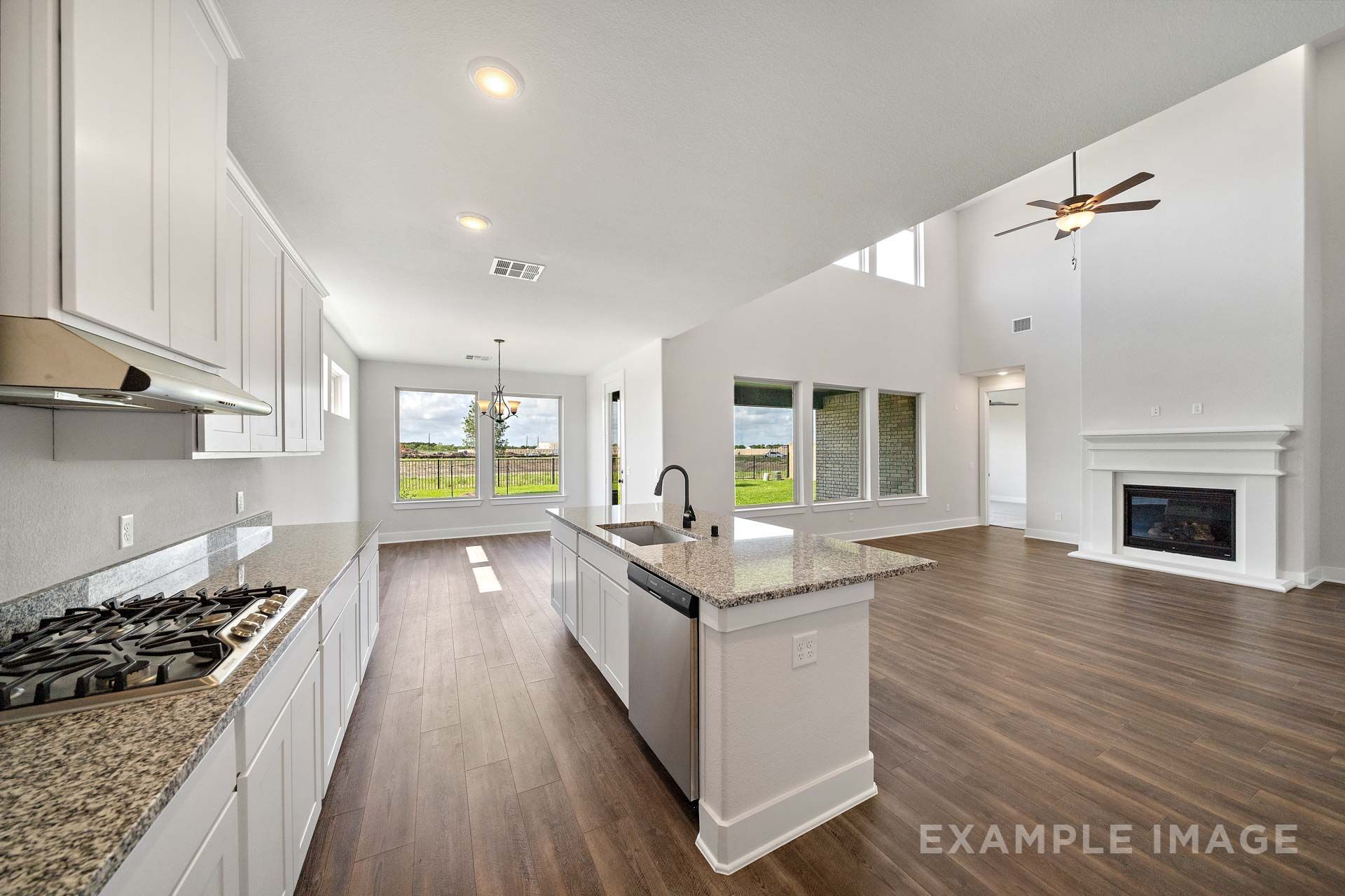 Open-concept kitchen and living area in The Victoria by Davidson Homes, featuring white cabinetry, granite island, and fireplace.