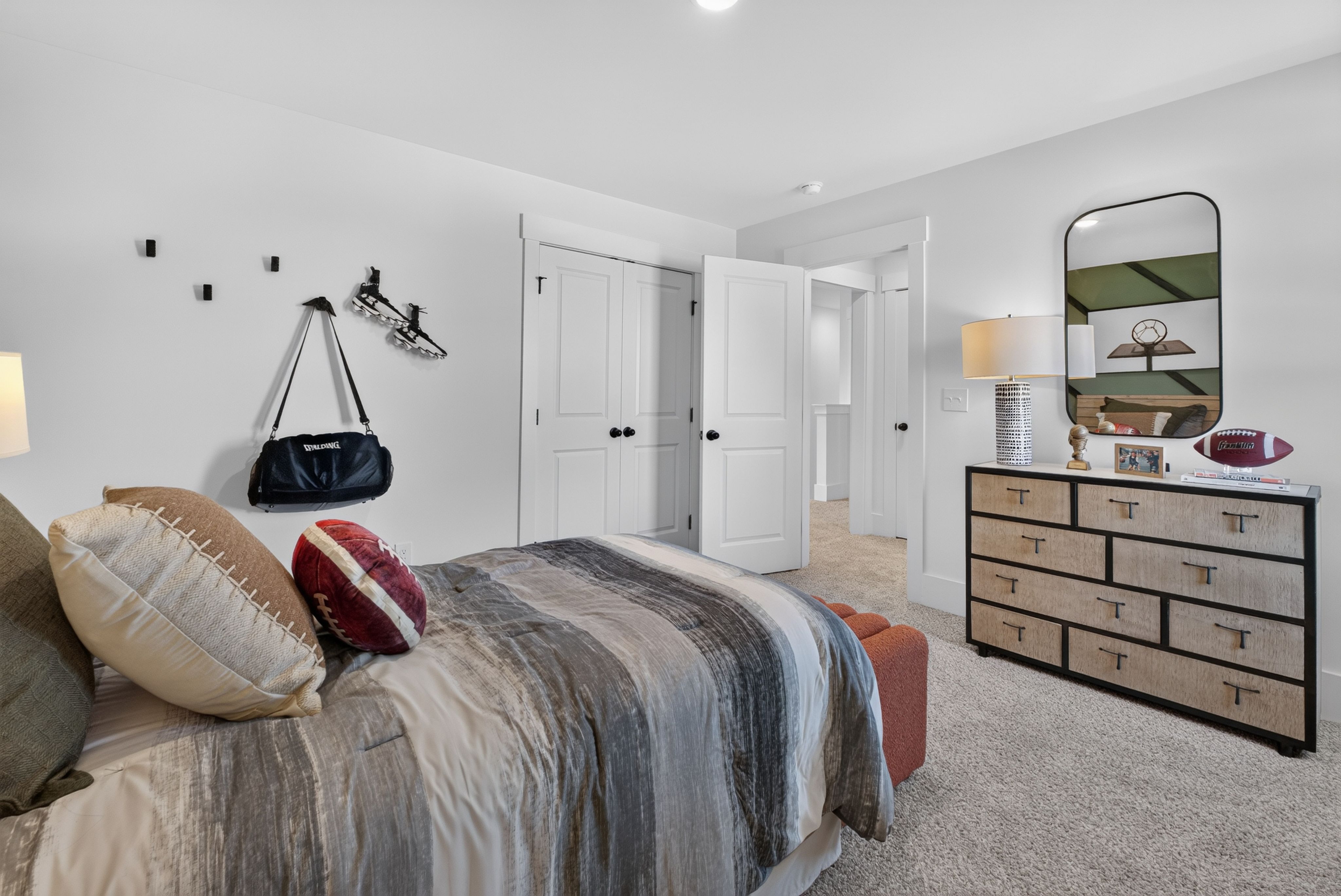 Sports-themed bedroom with football pillows and wood dresser at Evergreen Mill by Davidson Homes in Madison, Alabama