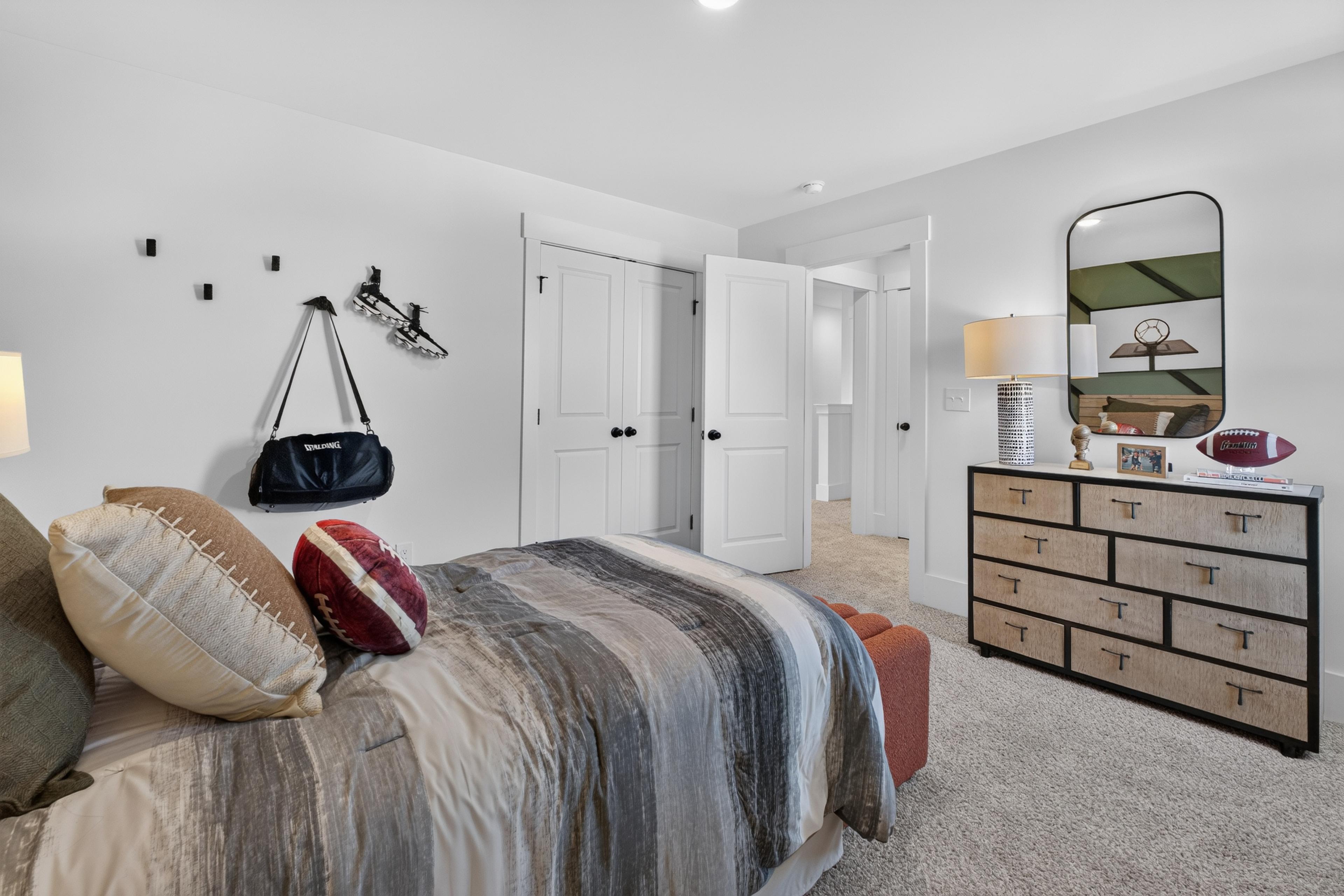 Sports-themed bedroom with football pillows and wood dresser at Evergreen Mill by Davidson Homes in Madison, Alabama