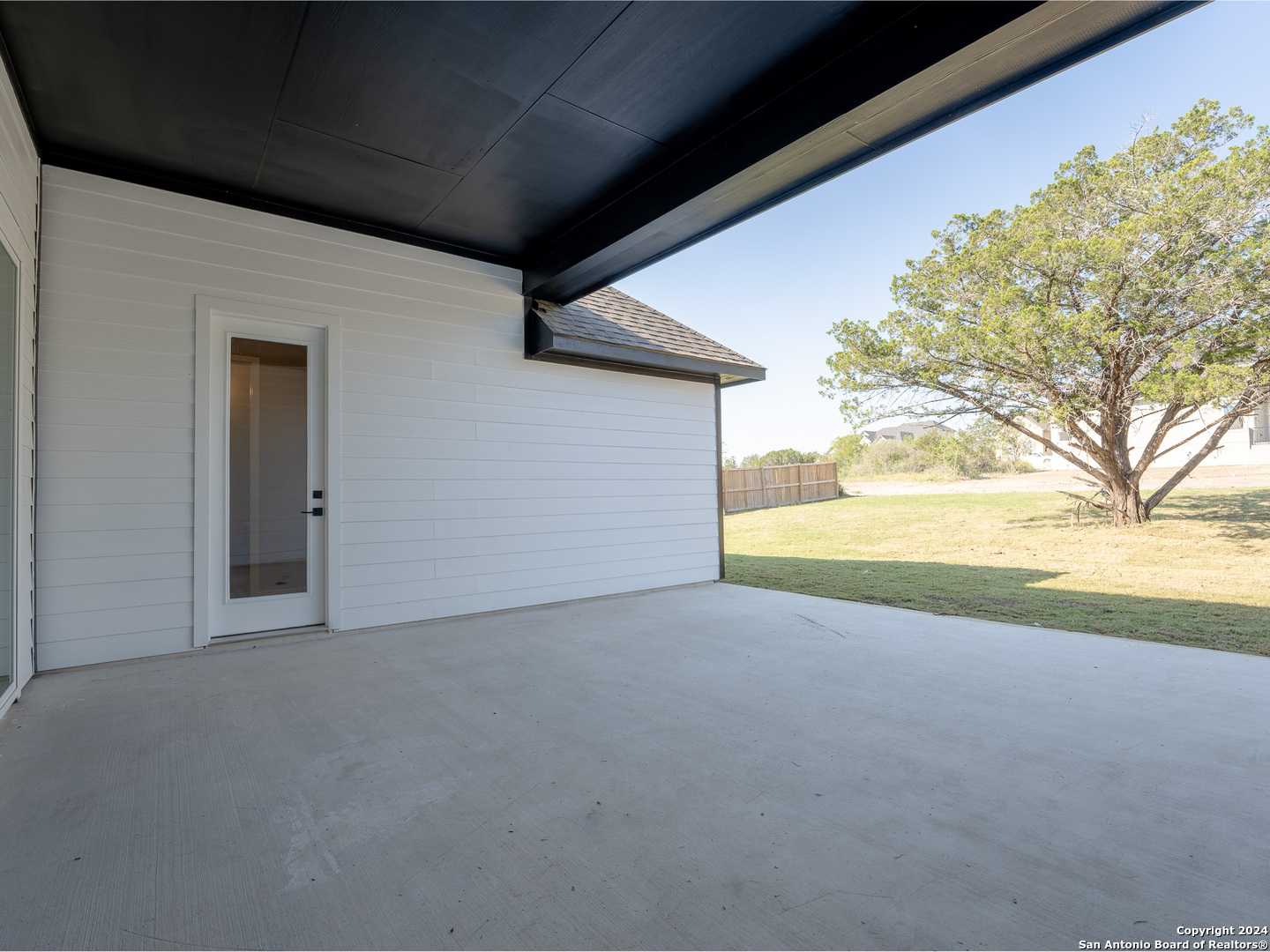 Covered back patio with black ceiling and glass door in Davidson Homes The Summerlin A, grassy yard and oak tree in Potranco Oaks, Castroville, Texas