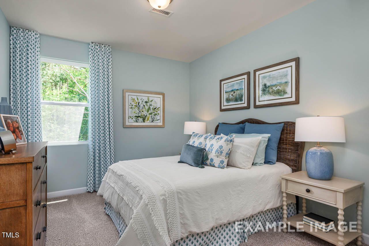 Cozy light blue bedroom with queen bed, rattan headboard, dresser, lamps, and artwork in Davidson Homes The Willow G, Angier, NC