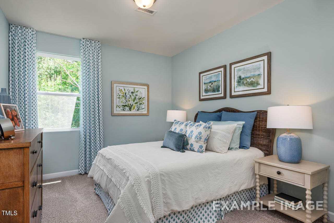 Cozy light blue bedroom with rattan headboard bed, blue pillows, and framed artwork in Davidson Homes The Willow C, Angier, NC