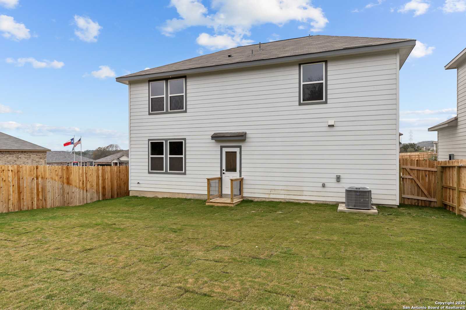 Backyard view of two-story Davidson Homes Murray I with covered deck, wooden fence, and grassy lawn in Royal Crest, San Antonio, Texas