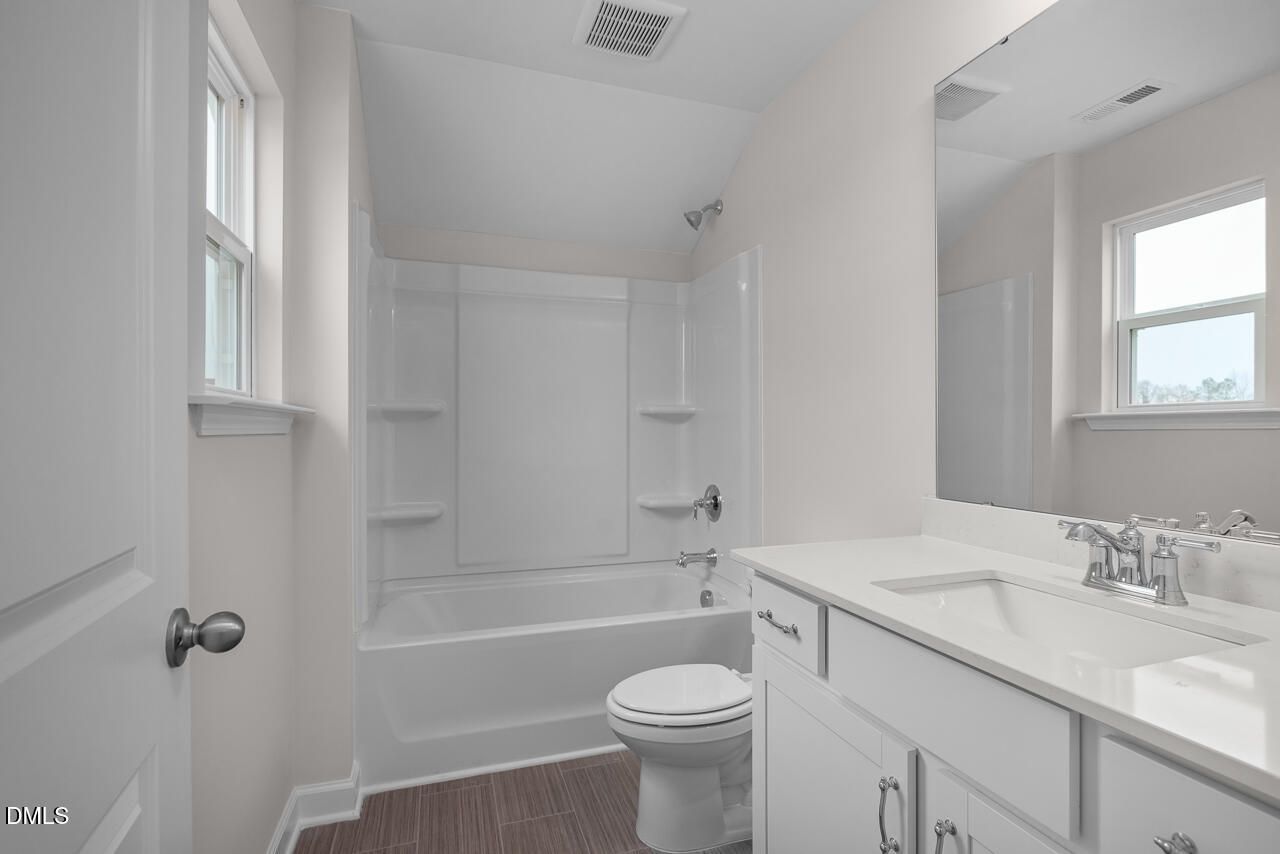 Bright bathroom with white subway tile tub-shower, single vanity sink, toilet, and window in Davidson Homes The Cypress D II, Angier, NC