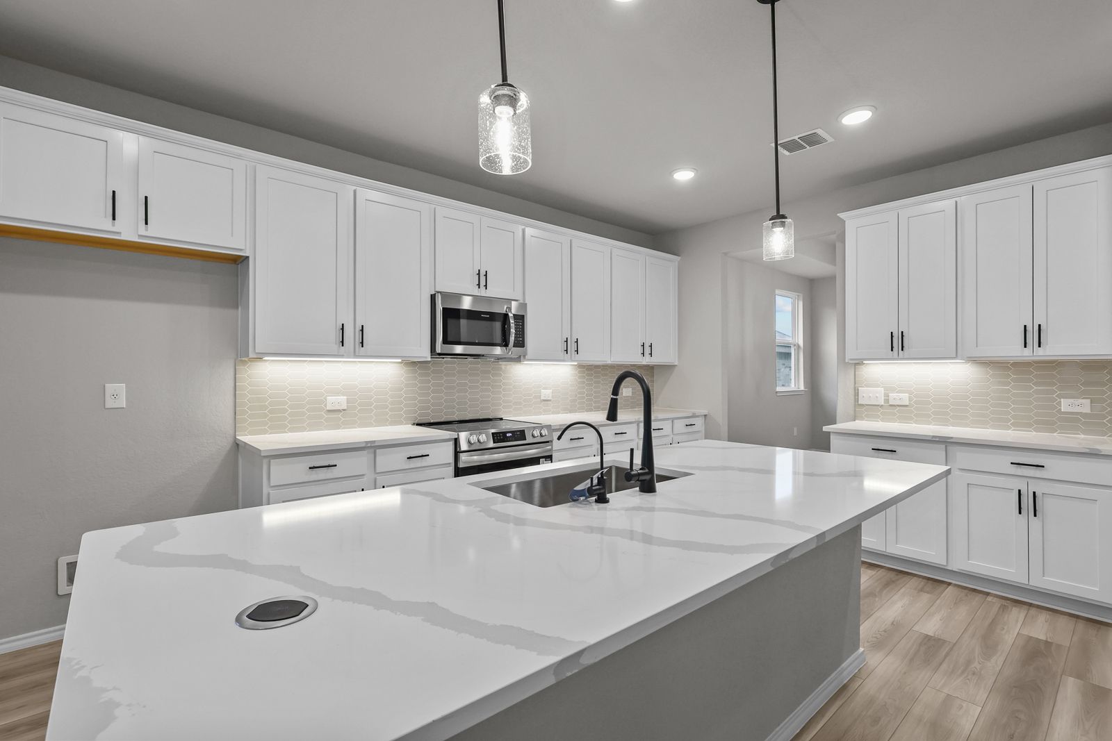 Modern kitchen in The Glenwood E featuring white cabinets, quartz countertops, a large island, and stainless appliances.