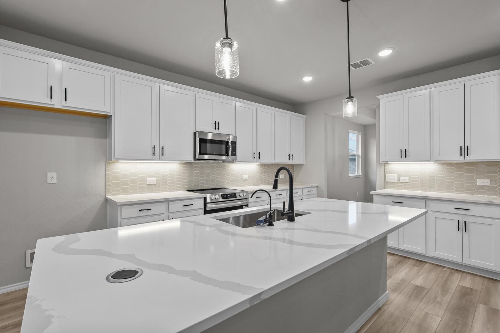 Modern kitchen in The Glenwood E featuring white cabinets, quartz countertops, a large island, and stainless appliances.