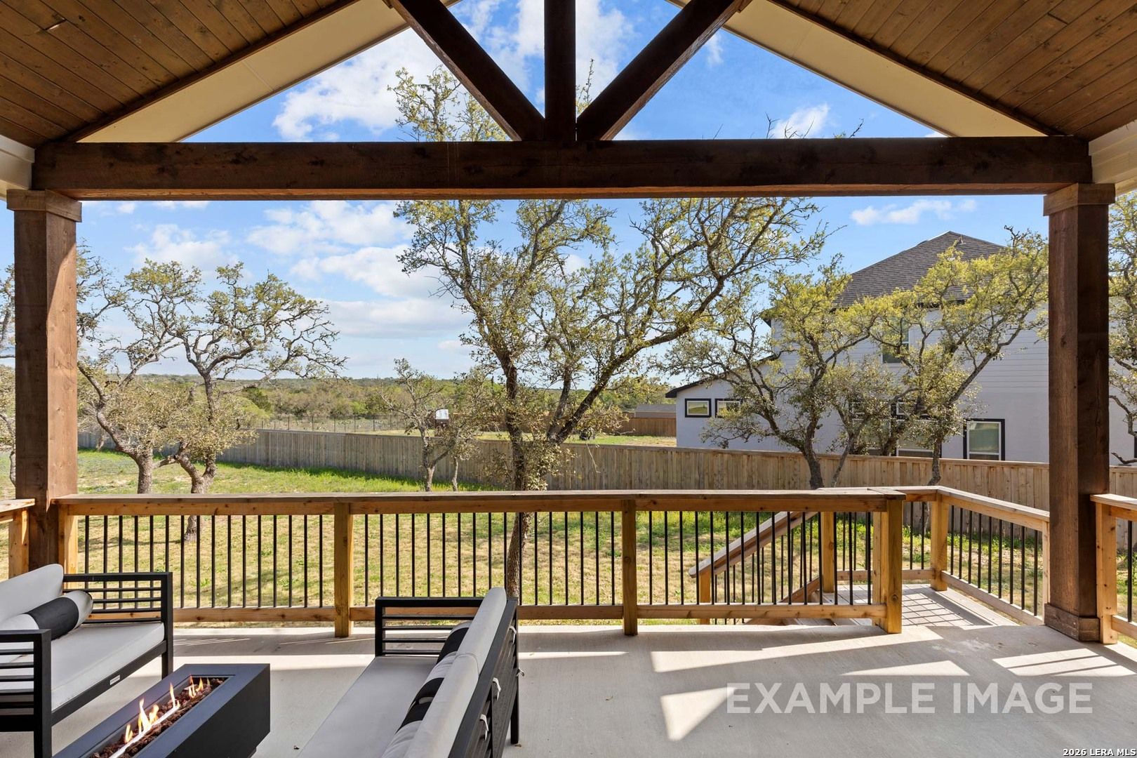 Covered outdoor patio with wood beams and fire pit overlooking the backyard in The Reserve at Potranco Oaks, Castroville.