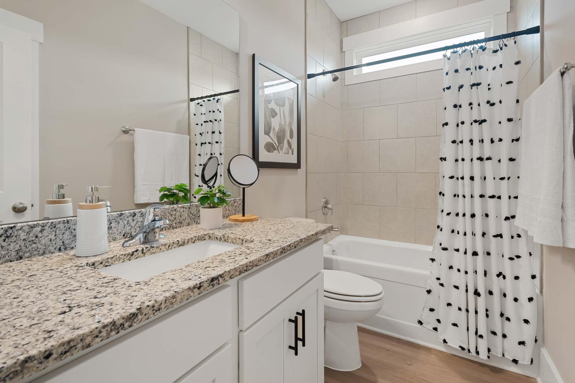 Spacious modern bathroom at Durham Farms in Harvest, Alabama with granite vanity, soaking tub, and polka dot shower curtain
