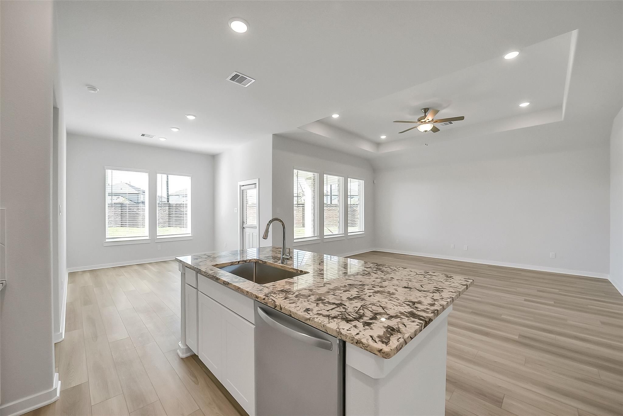 Modern open-concept kitchen featuring granite island, stainless sink, and white cabinets in The Acadia A floor plan, Katy, Texas